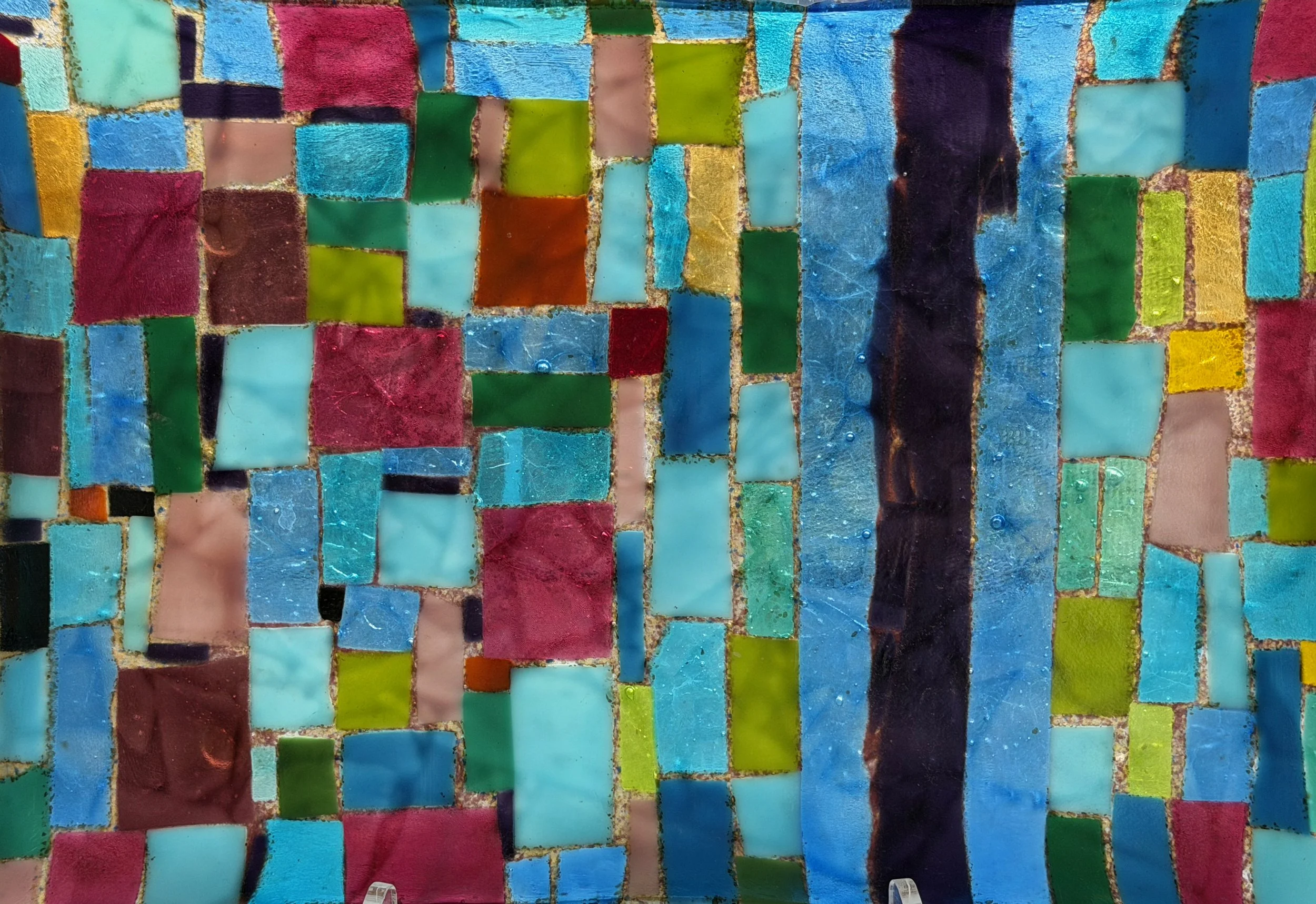 A colorful mosaic made of small, irregularly shaped tiles in shades of blue, green, red, pink, yellow, black, and brown.