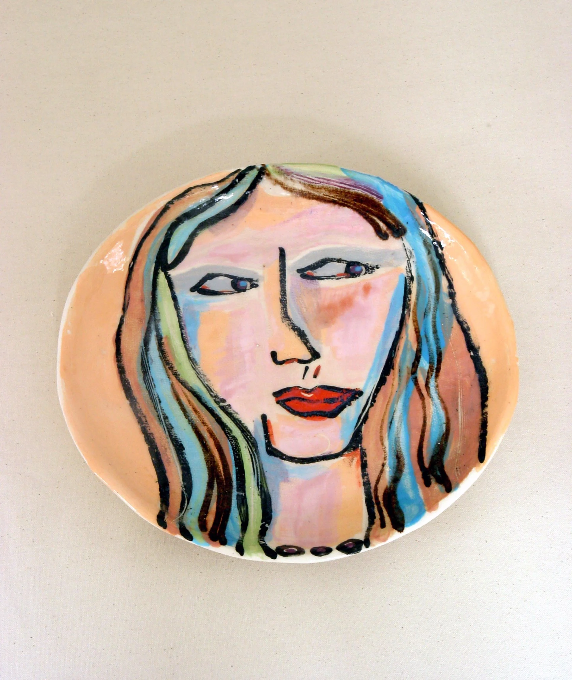 Decorative circular plate with a colorful abstract portrait of a woman with long hair, painted with expressive brushstrokes and vibrant colors.