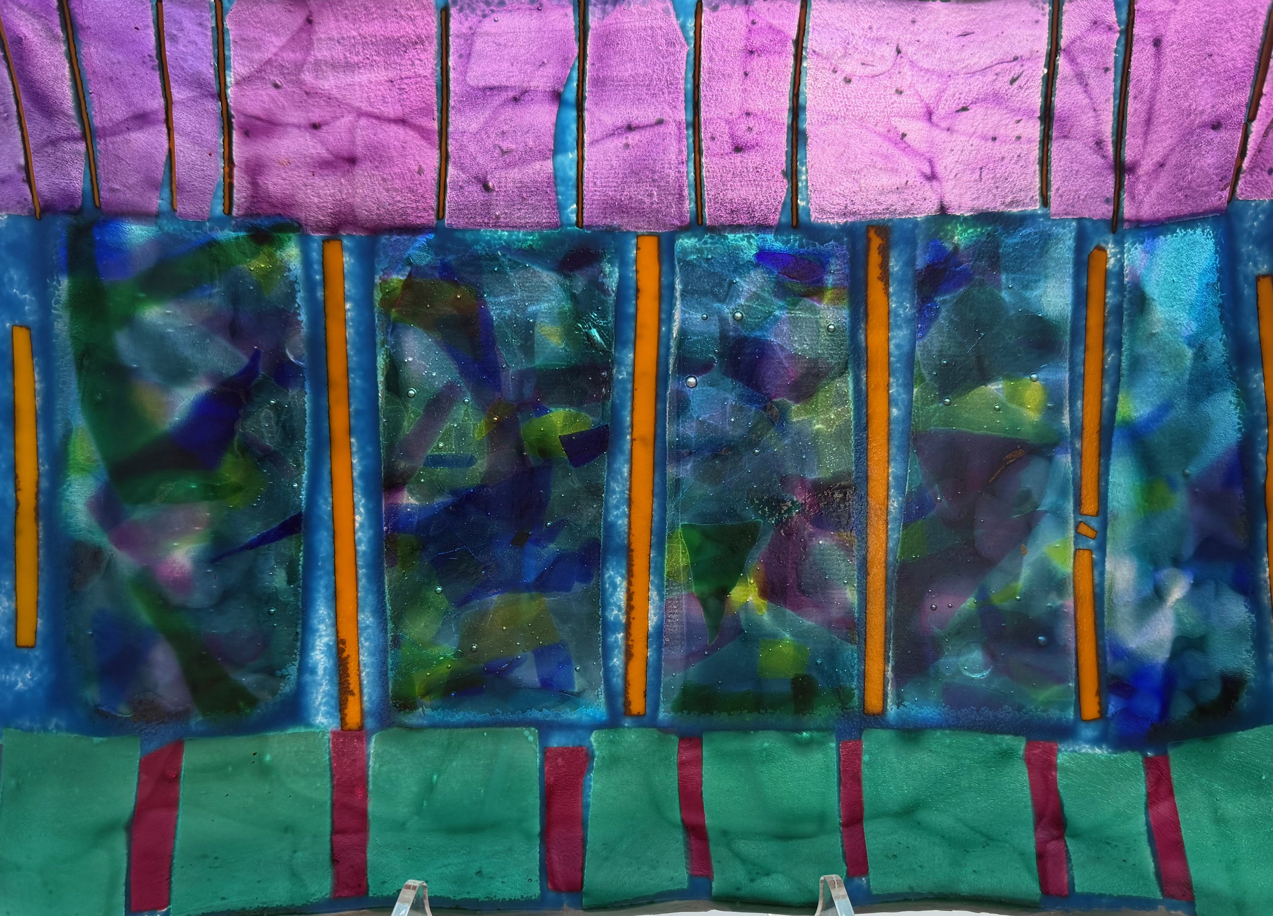 Colorful stained glass window with abstract designs in shades of purple, green, blue, and orange, divided into segments by orange lines.