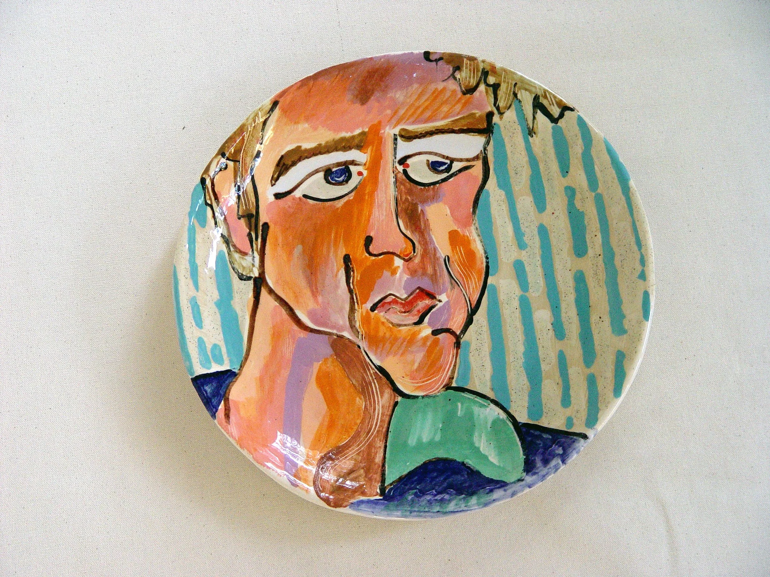 Decorative ceramic plate featuring an abstract portrait of a woman with short hair, painted in bright, contrasting colors and bold black outlines.