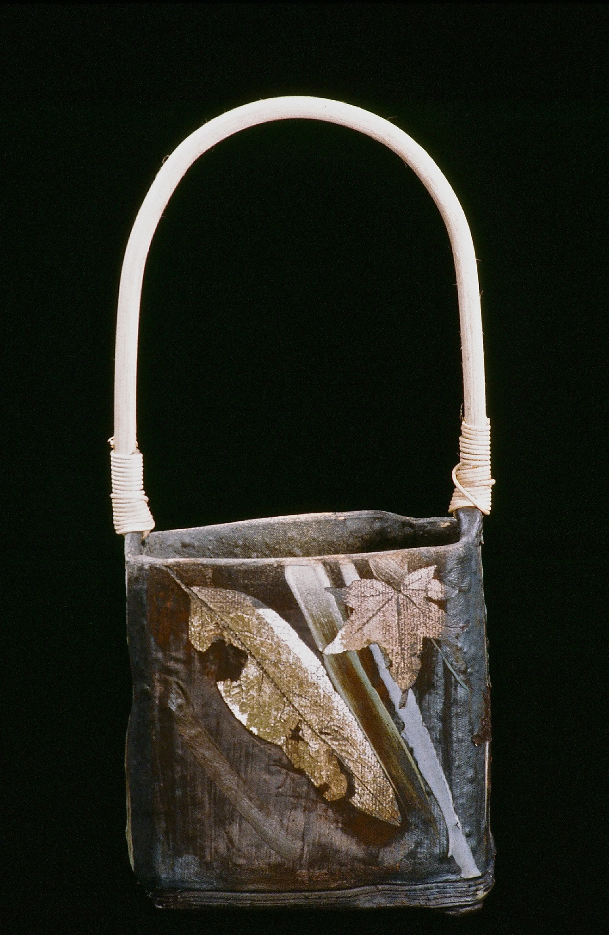 A handmade handbag made from natural materials, decorated with dried leaves and wood, with a curved light-colored handle.