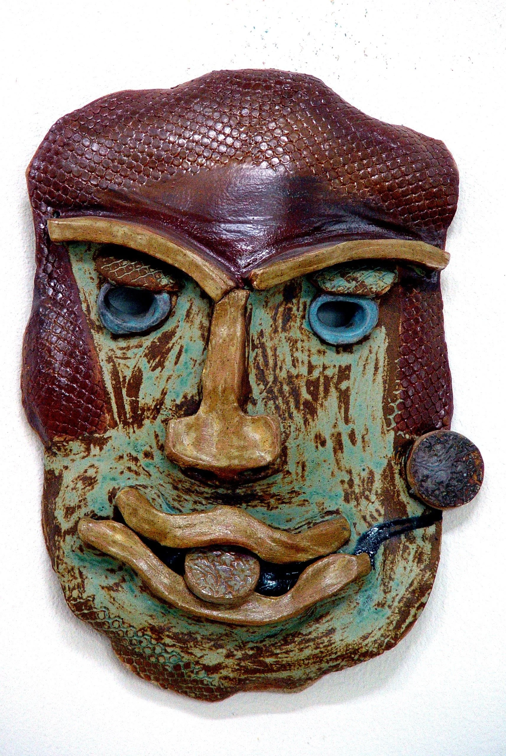 Colorful, textured mask resembling a human face with prominent lips, nose, and eyes, made of various materials.