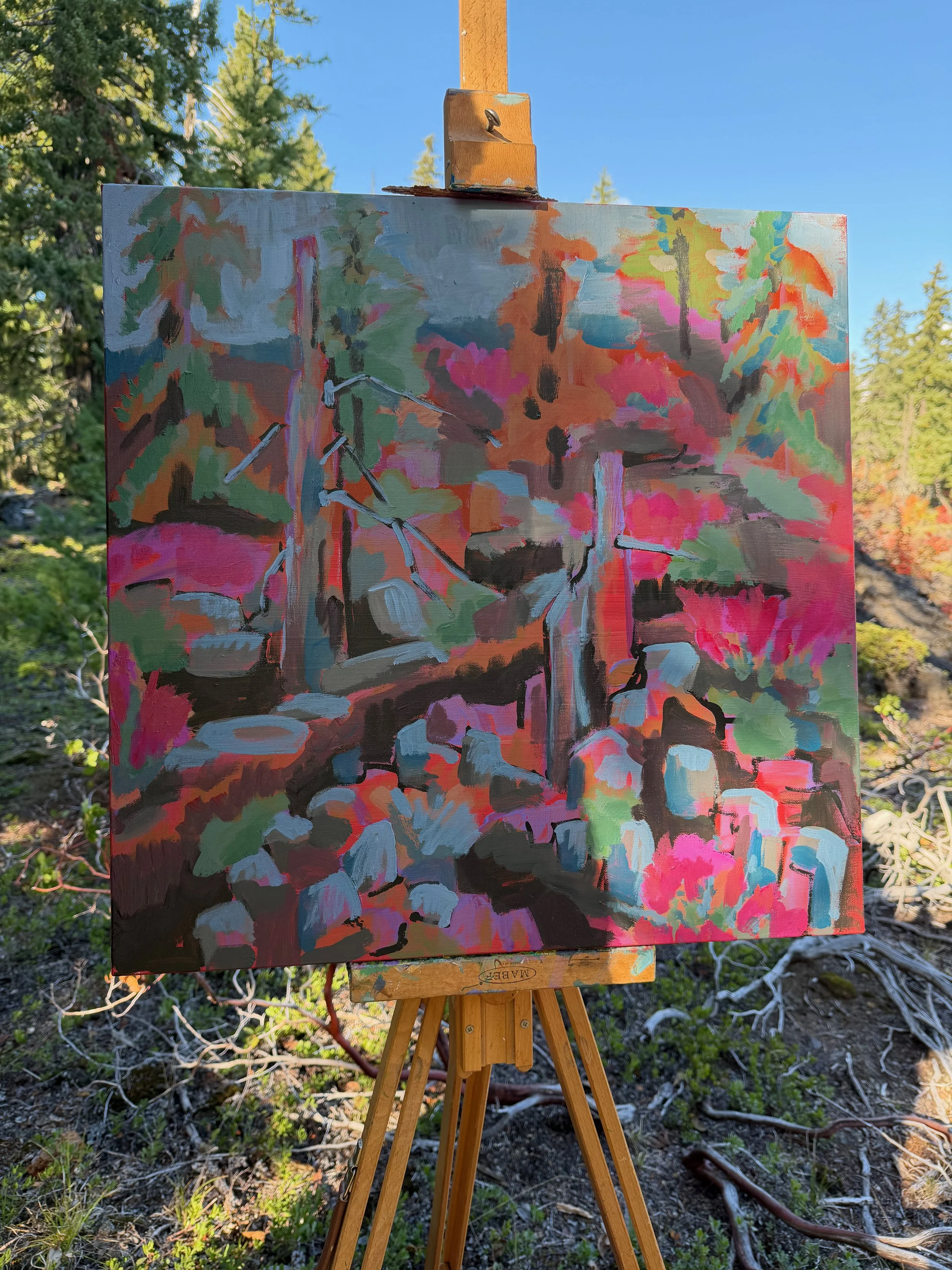 An impressionistic painting of a forest scene with trees, rocks, and a small creek or waterfall, featuring vibrant pink, green, and blue hues, set outdoors with a backdrop of a clear blue sky and trees.