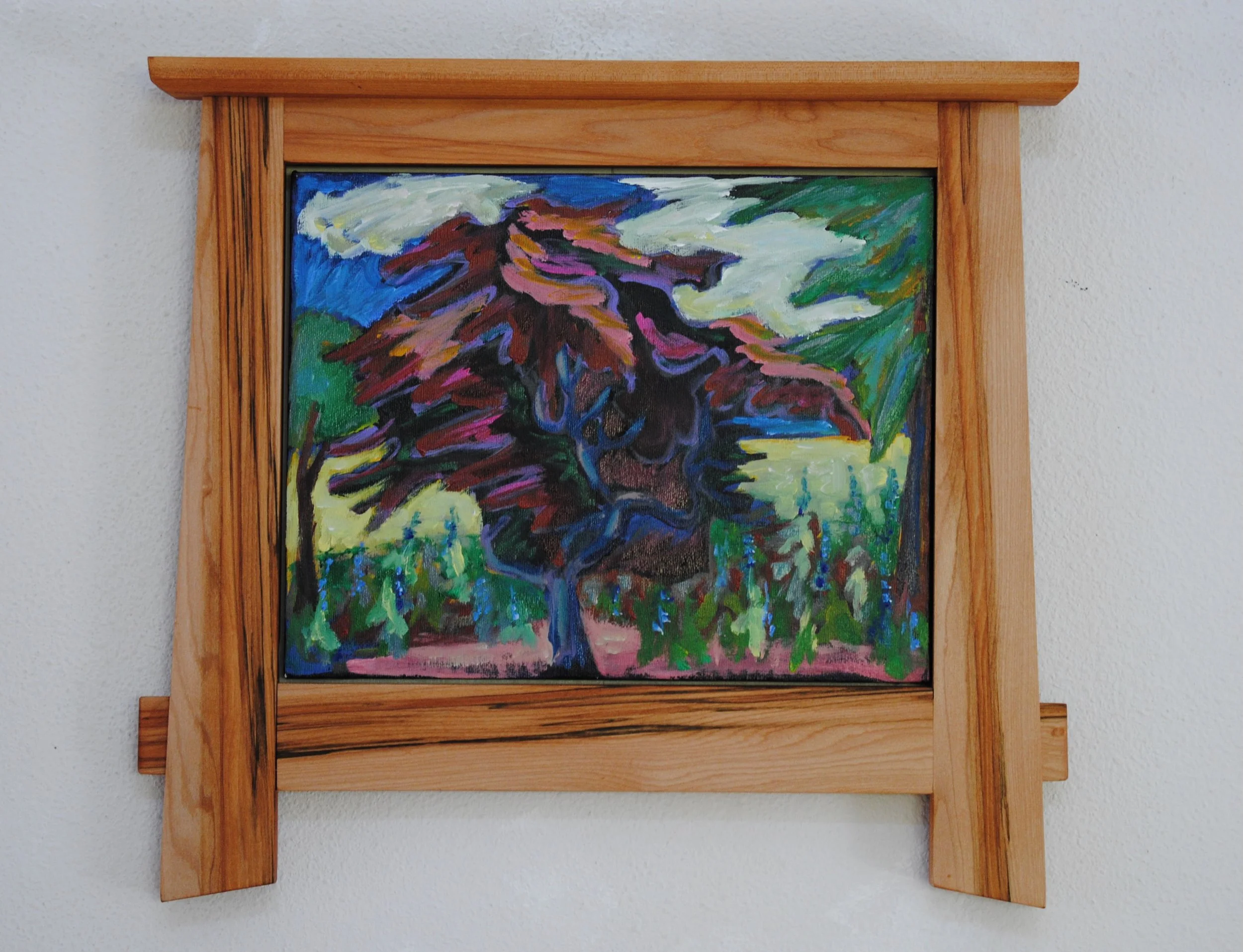 Colorful painting of a tree with purple, red, and brown leaves, set in a wooden frame on a white wall.