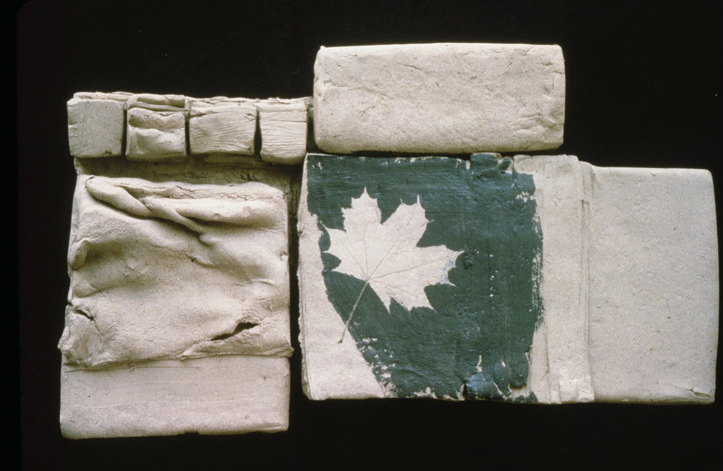 A collection of six ceramic tiles, one of which features a painted green and white maple leaf design.