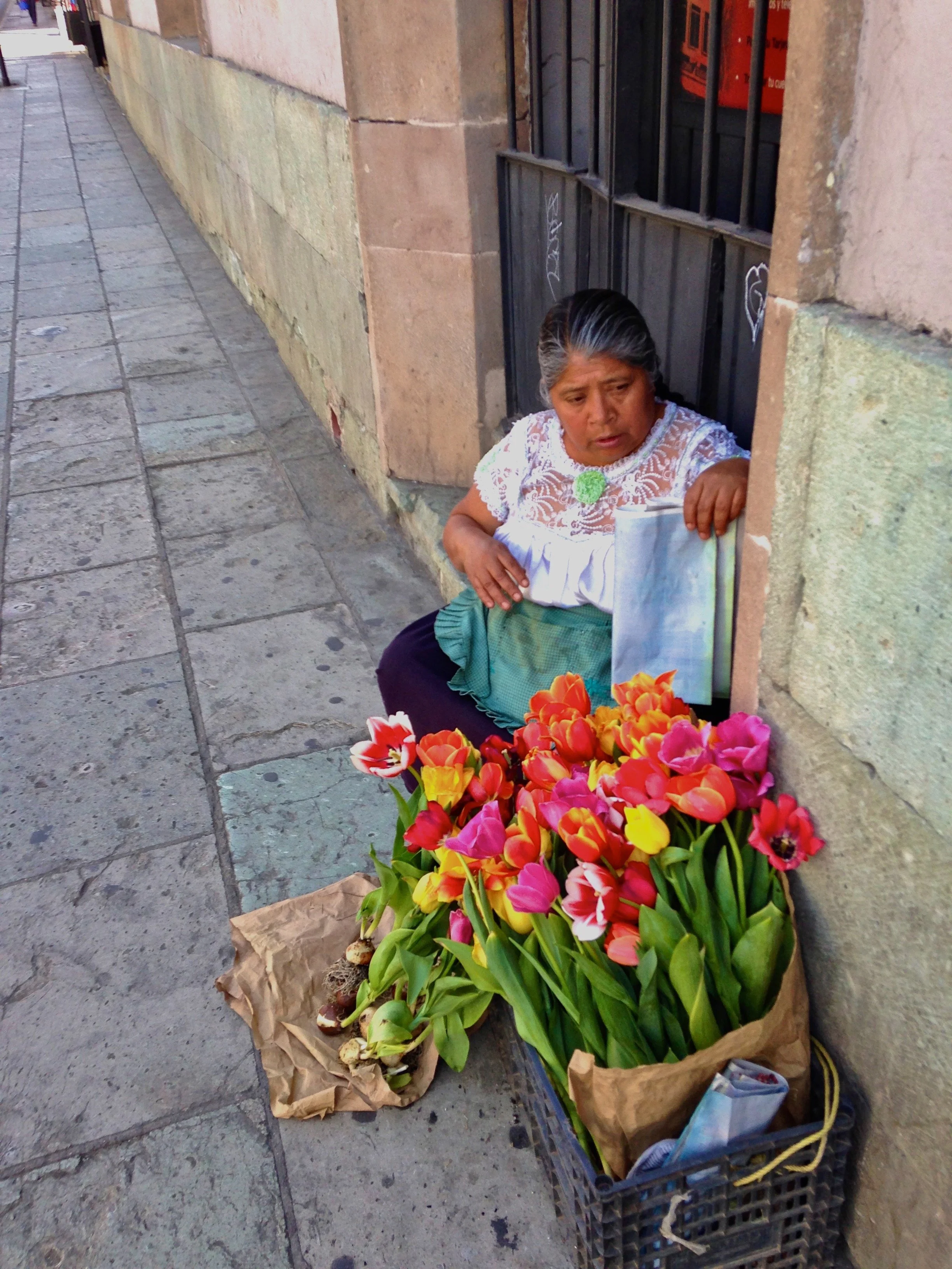 A woman selling colorful tulips on a city sidewalk.