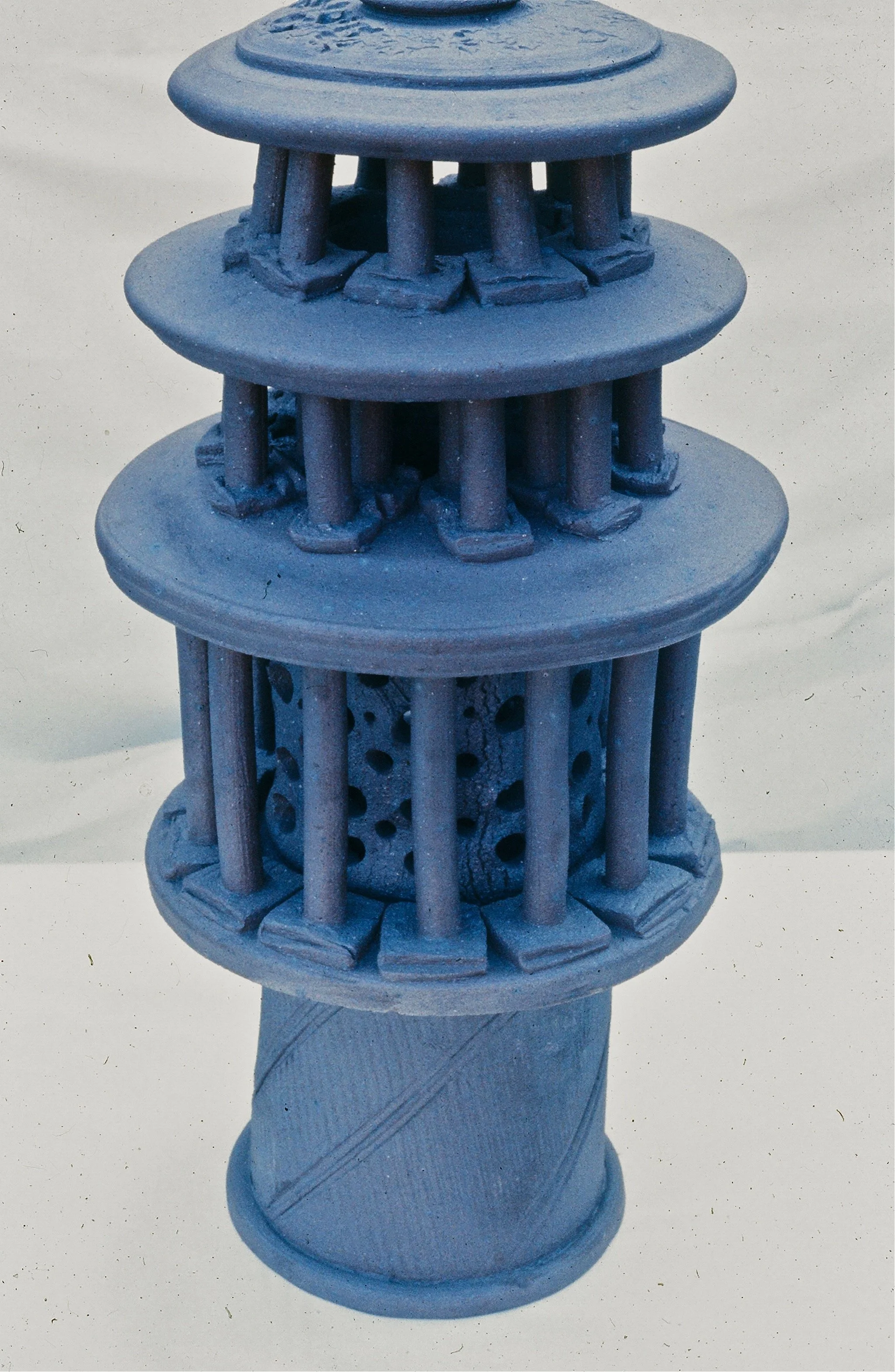 A blue model of a lighthouse with three tiers, featuring detailed railings and a round base.