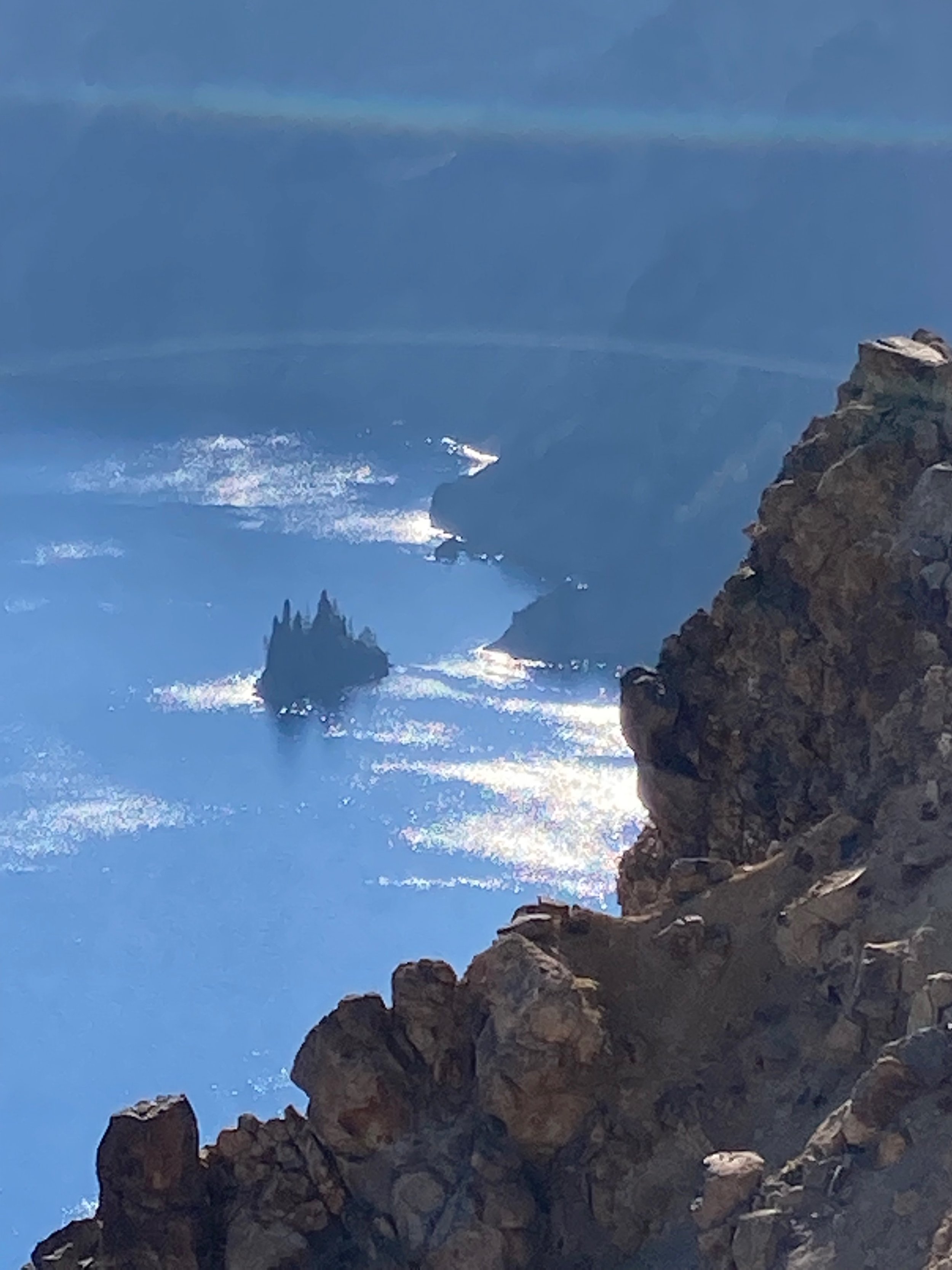 Aerial view of a lake with small islands and rocky cliffs, with blue waters and sunlight reflecting off the surface.