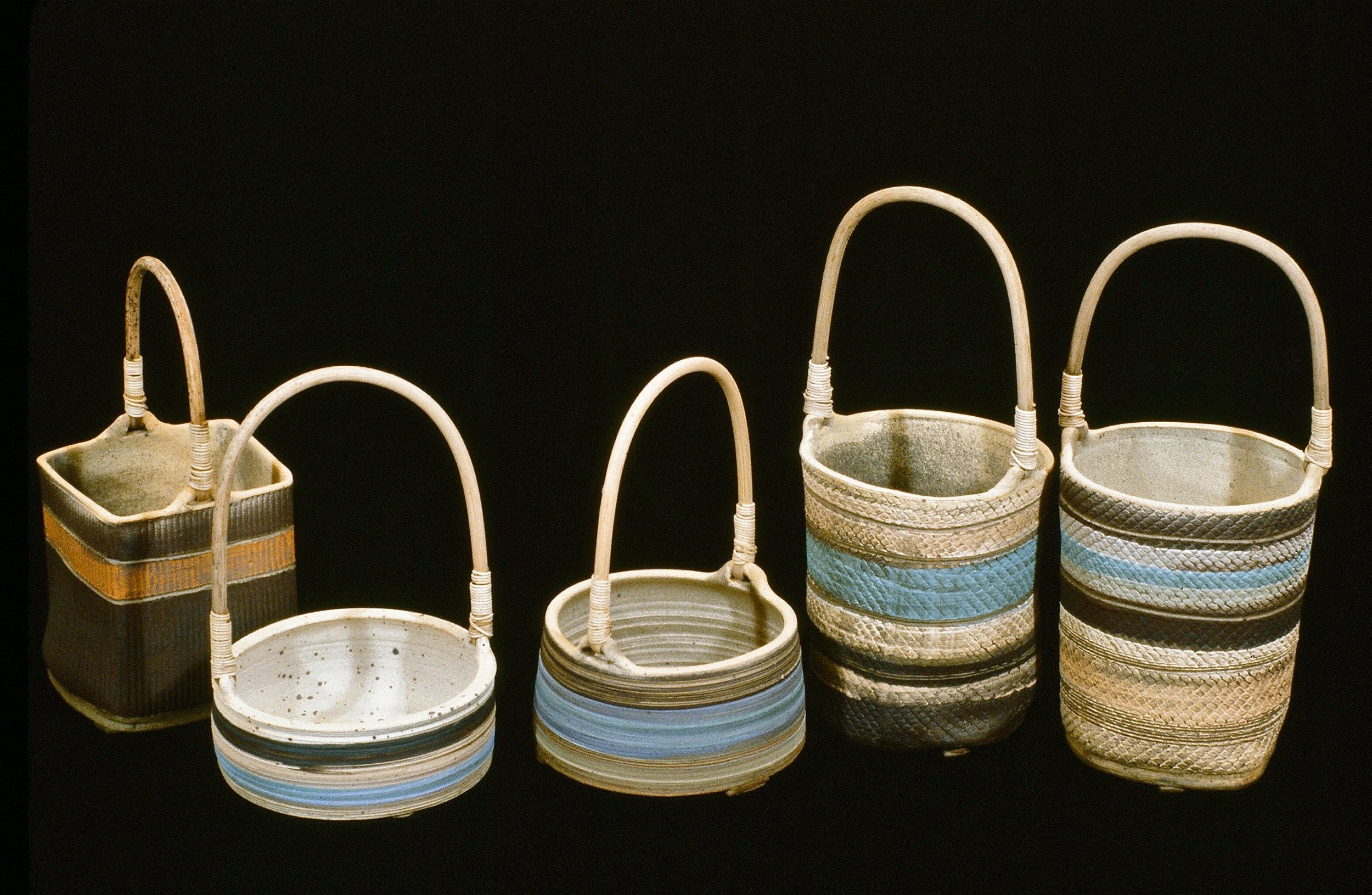 Five woven baskets with handles, varying in size and design, arranged in a line against a black background.