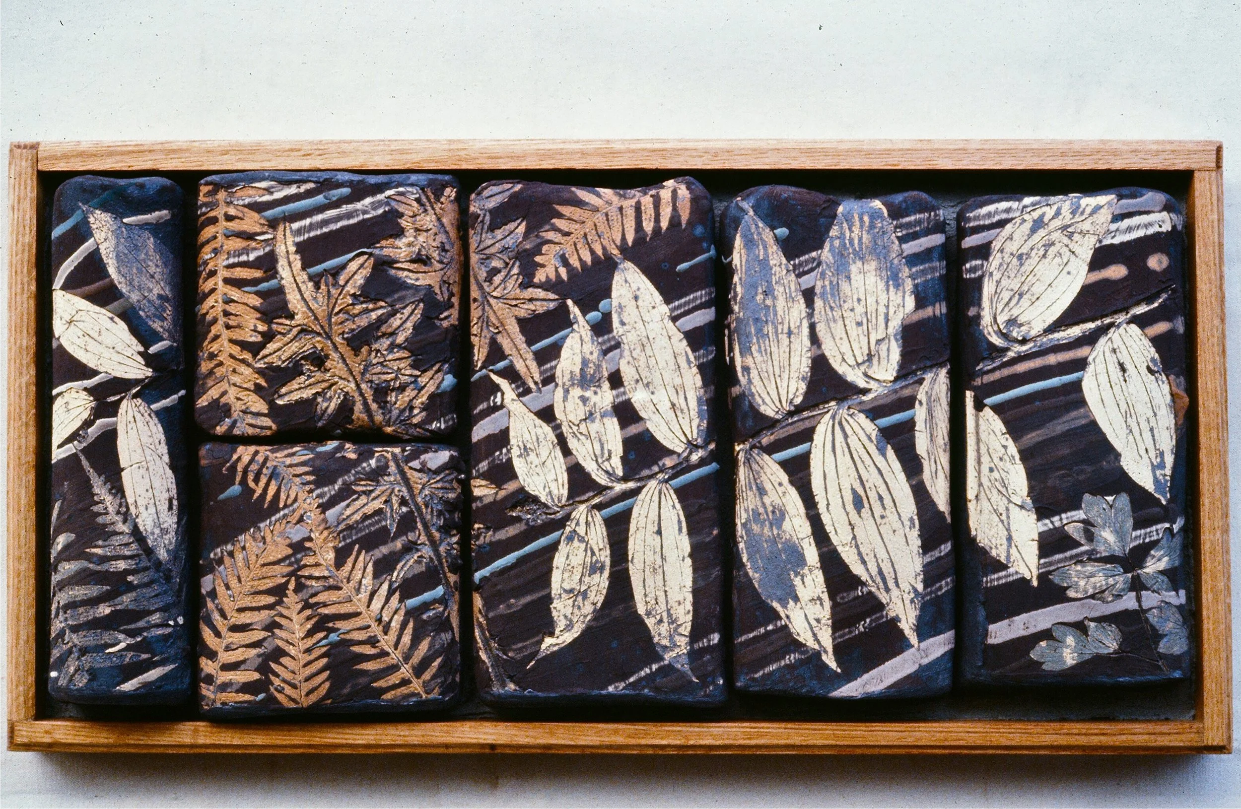 A wooden box containing ten rocks painted with black, white, and brown botanical leaf patterns.
