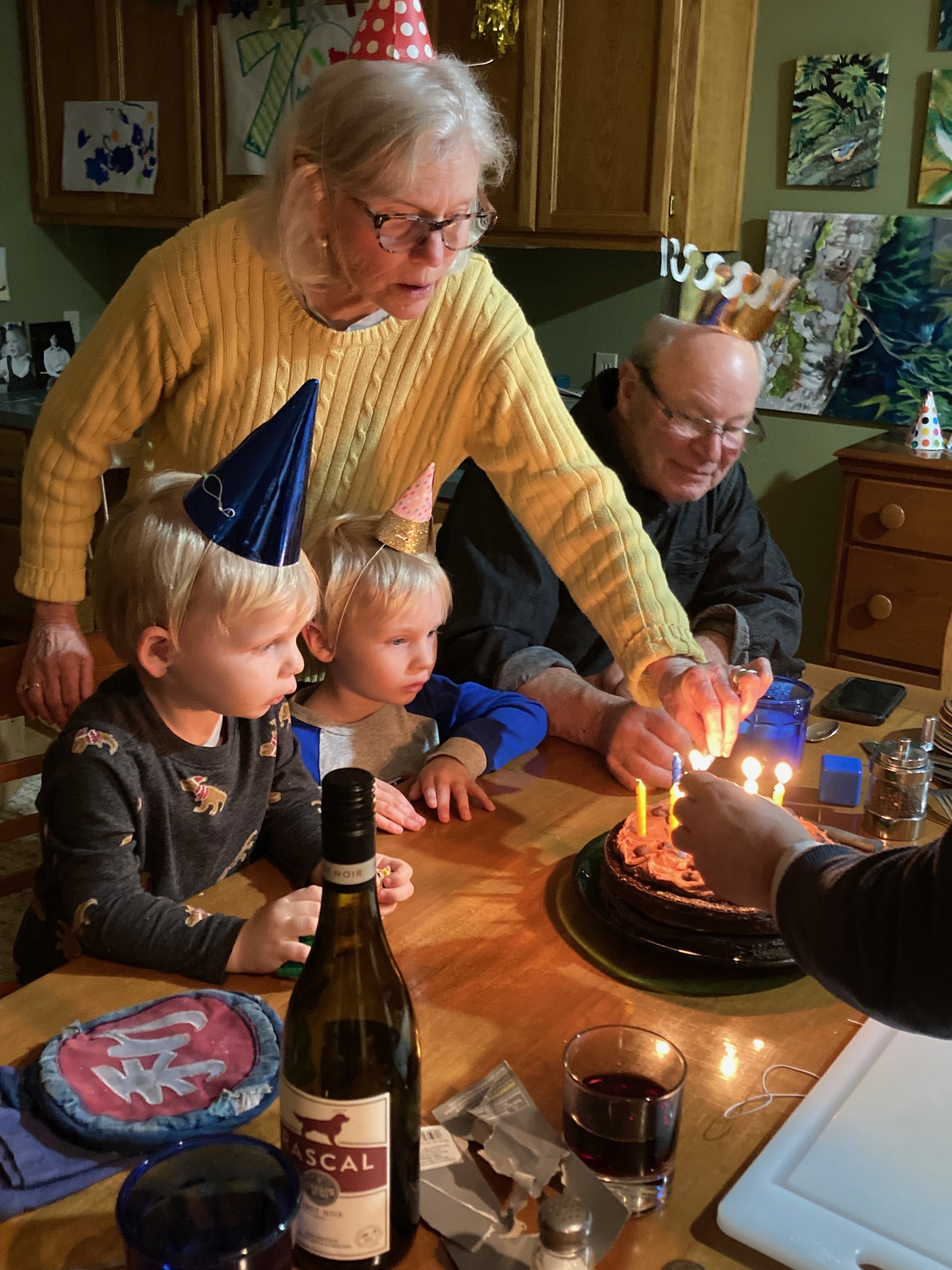 Family celebrating birthday with cake and candles, wearing party hats, in a cozy indoor setting.