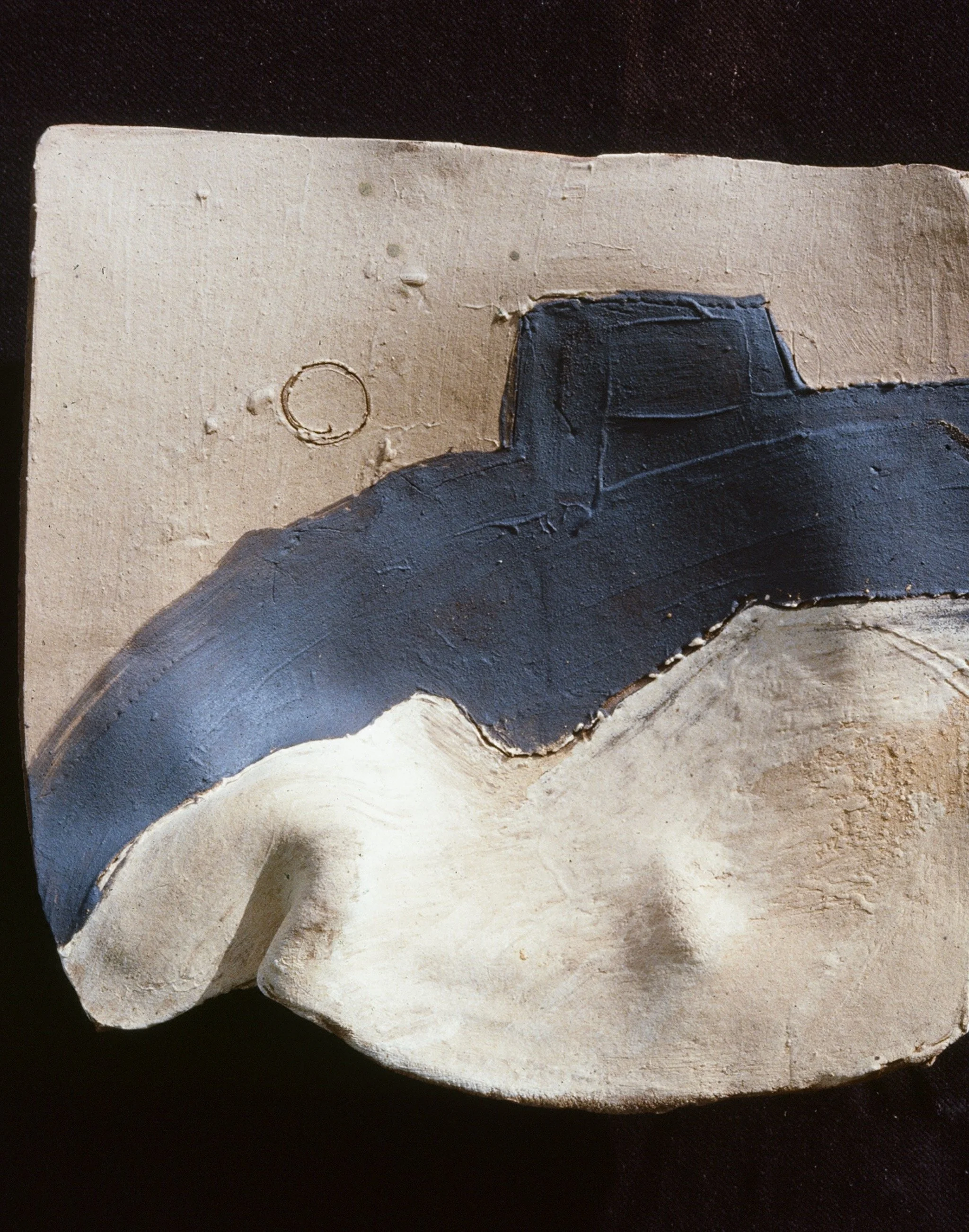 A textured, abstract sculpture or relief with a dark blue shape on a light beige background, showing rough and smooth surfaces.