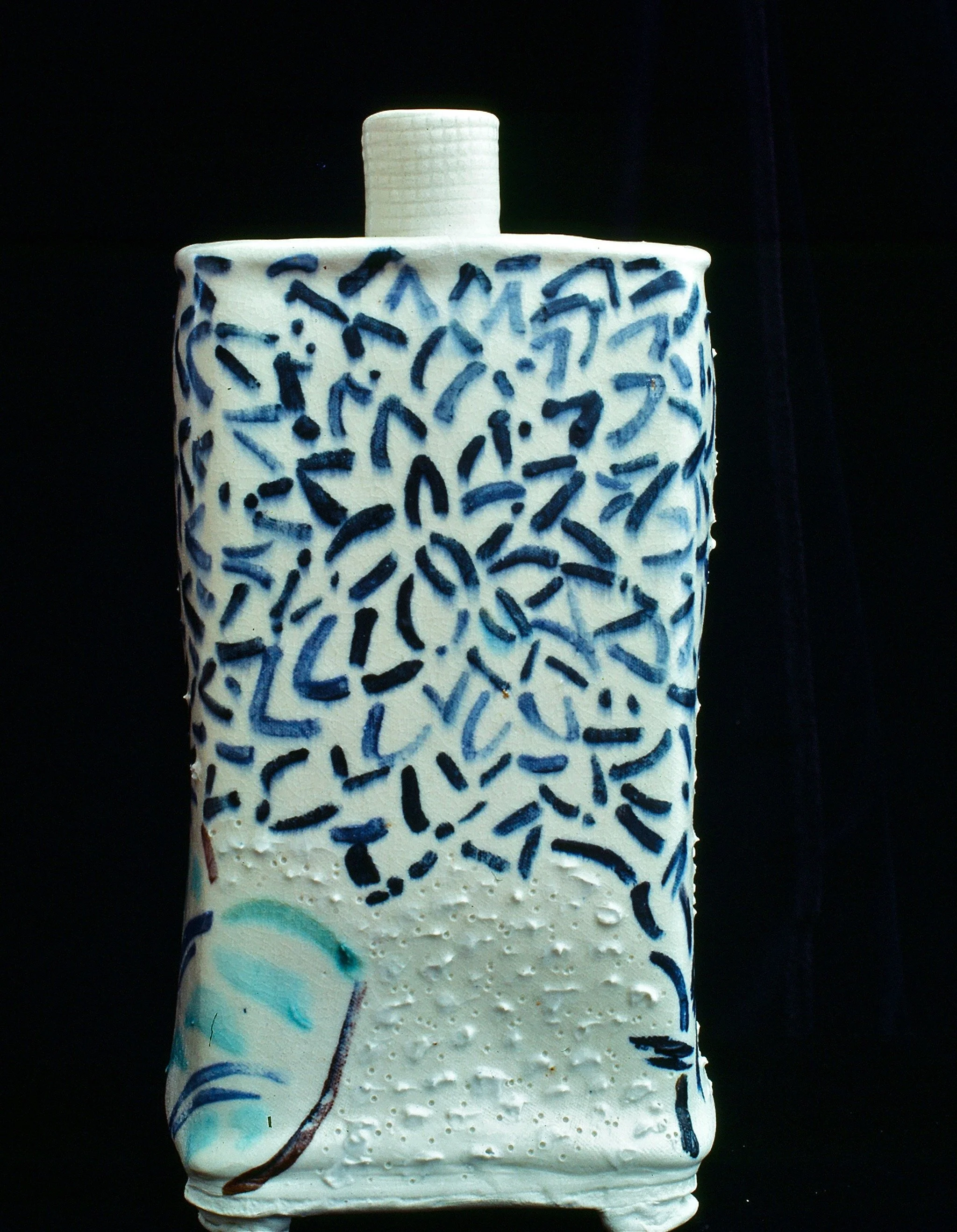 Ceramic sculpture resembling a perfume bottle with blue and black abstract patterns on a white background, and a small logo at the bottom left corner.