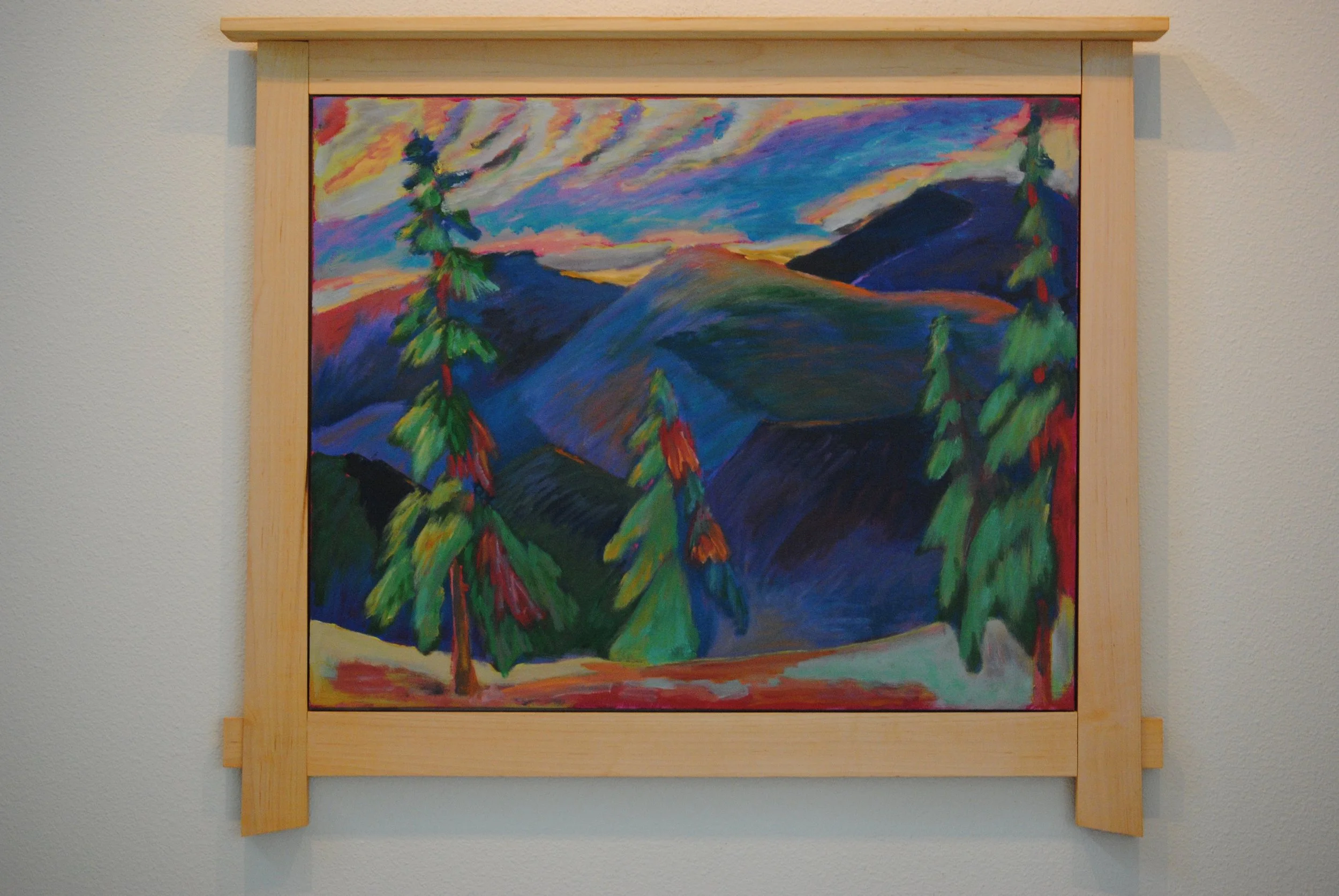Colorful landscape painting of mountains, trees, and a vibrant sky framed in light wood.