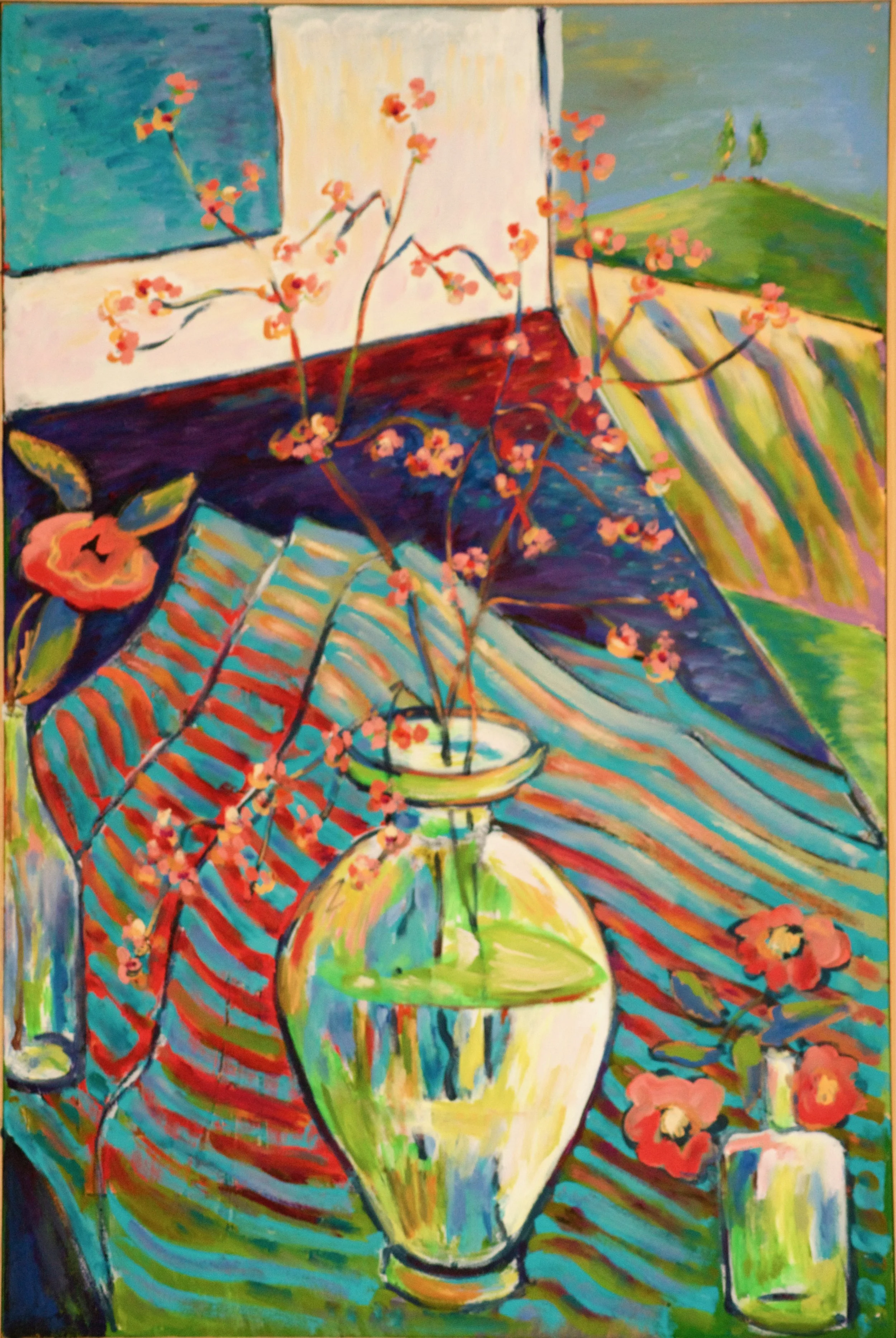 A colorful still life painting featuring a large yellow vase with floral branches, an orange flower, and a small bottle with red flowers on a striped cloth, with a landscape visible through a window in the background.