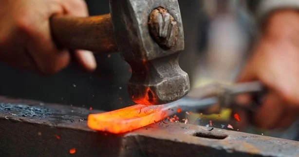 Blacksmith hammering hot metal on an anvil in a forge.