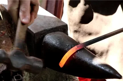 Blacksmith heating metal on an anvil using a hammer and glow from the forge.