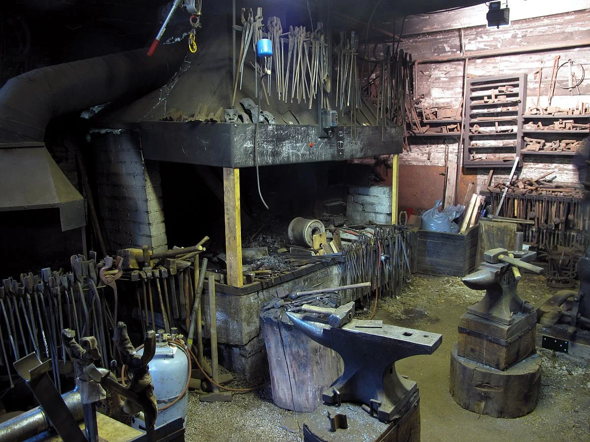 A blacksmith's workshop with tools hanging on the wall, a black forge, an anvil, and various metalworking tools and equipment.