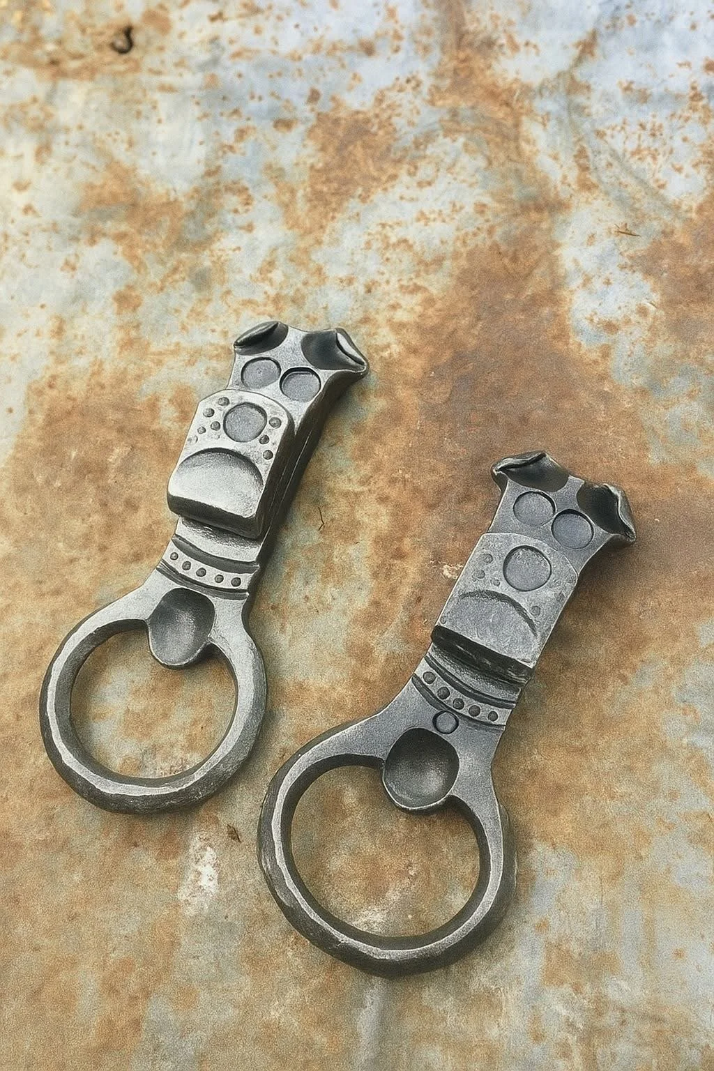 Two metallic brass knuckles shaped like gun triggers on a rusty surface.