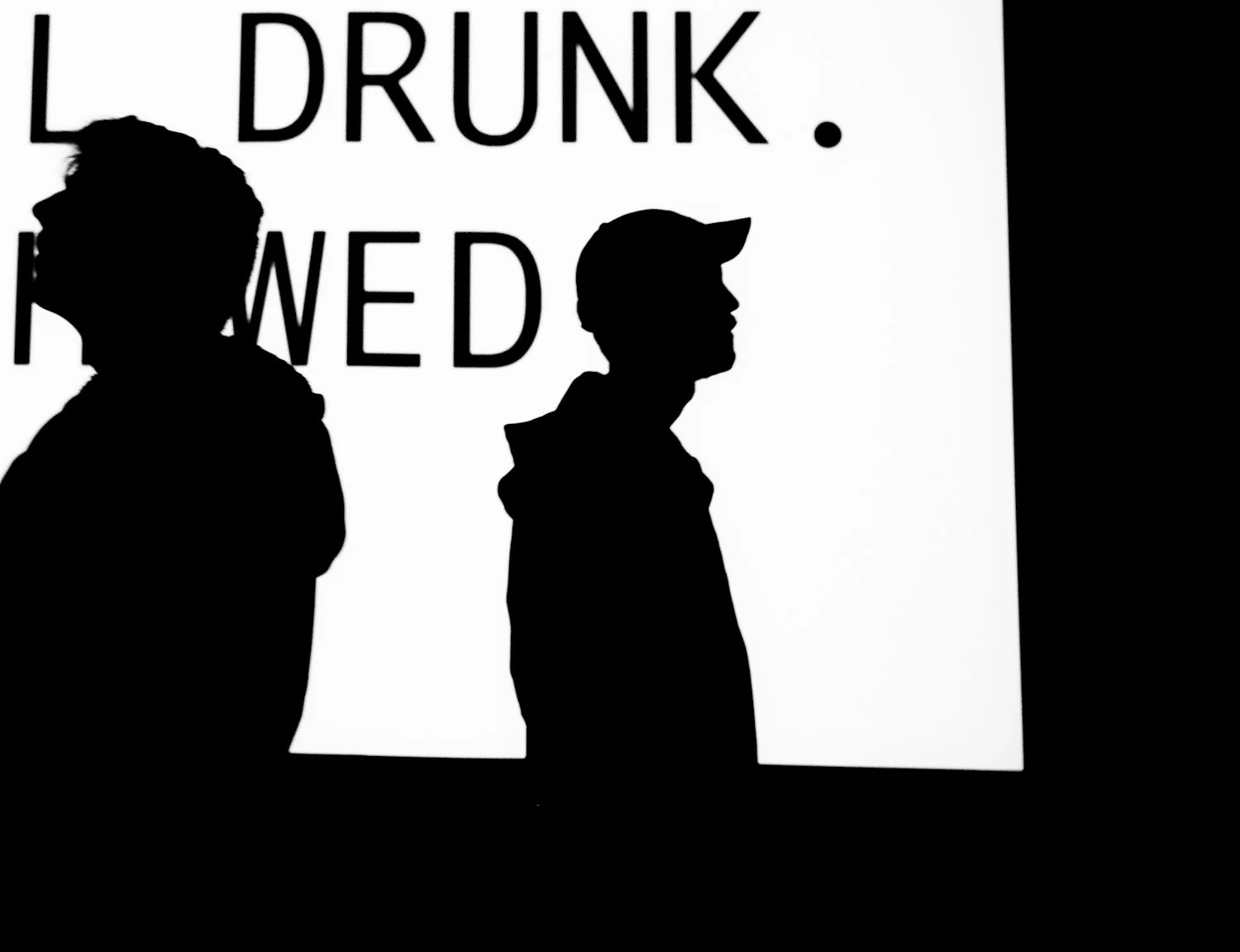 Silhouettes of two men standing in front of a backlit sign that reads "L DUNK WED".