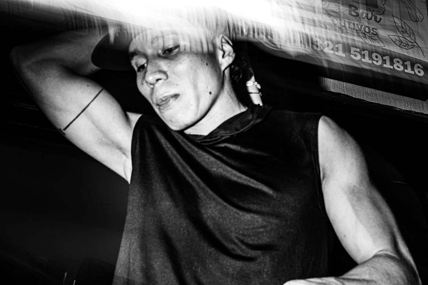 Black and white photo of a woman lying down with her arm behind her head, wearing a sleeveless top.