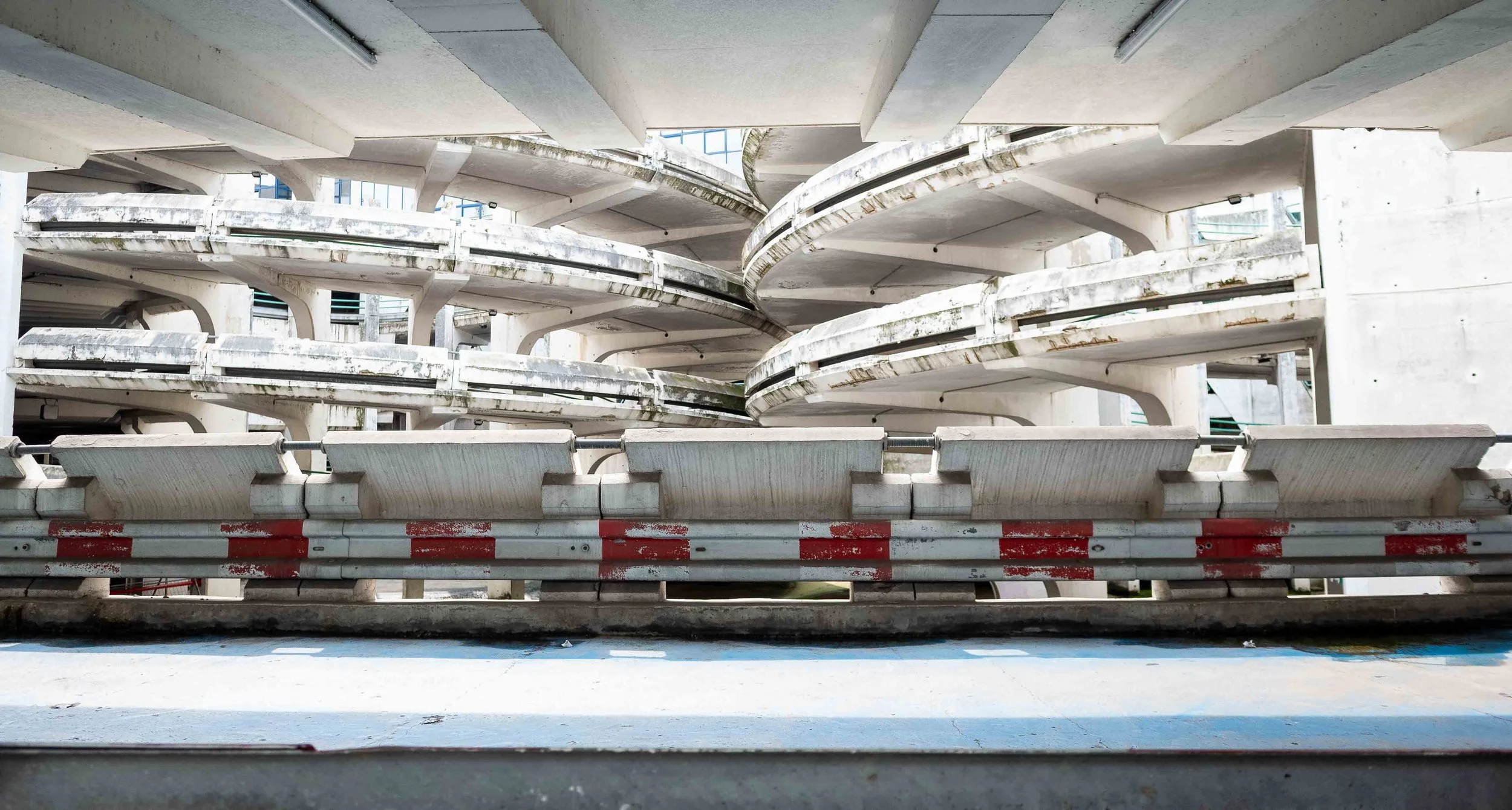 Multiple levels of a concrete parking garage with curved ramps and metal barriers at the top and bottom of the image.