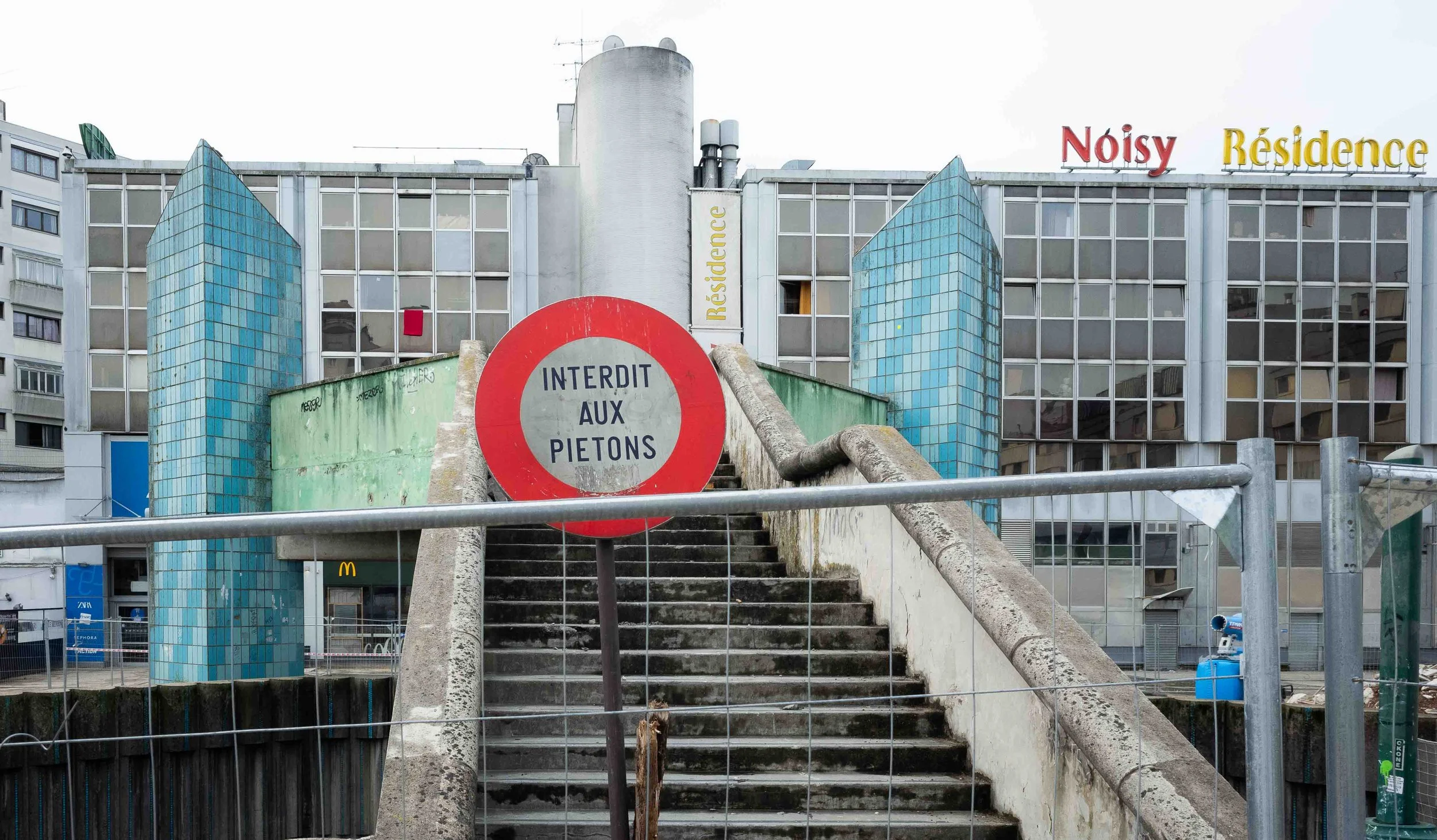 City building with stairs leading up, a sign that says 'Interdit aux piétons' and the words 'Noisy Résidence' on top of the building.