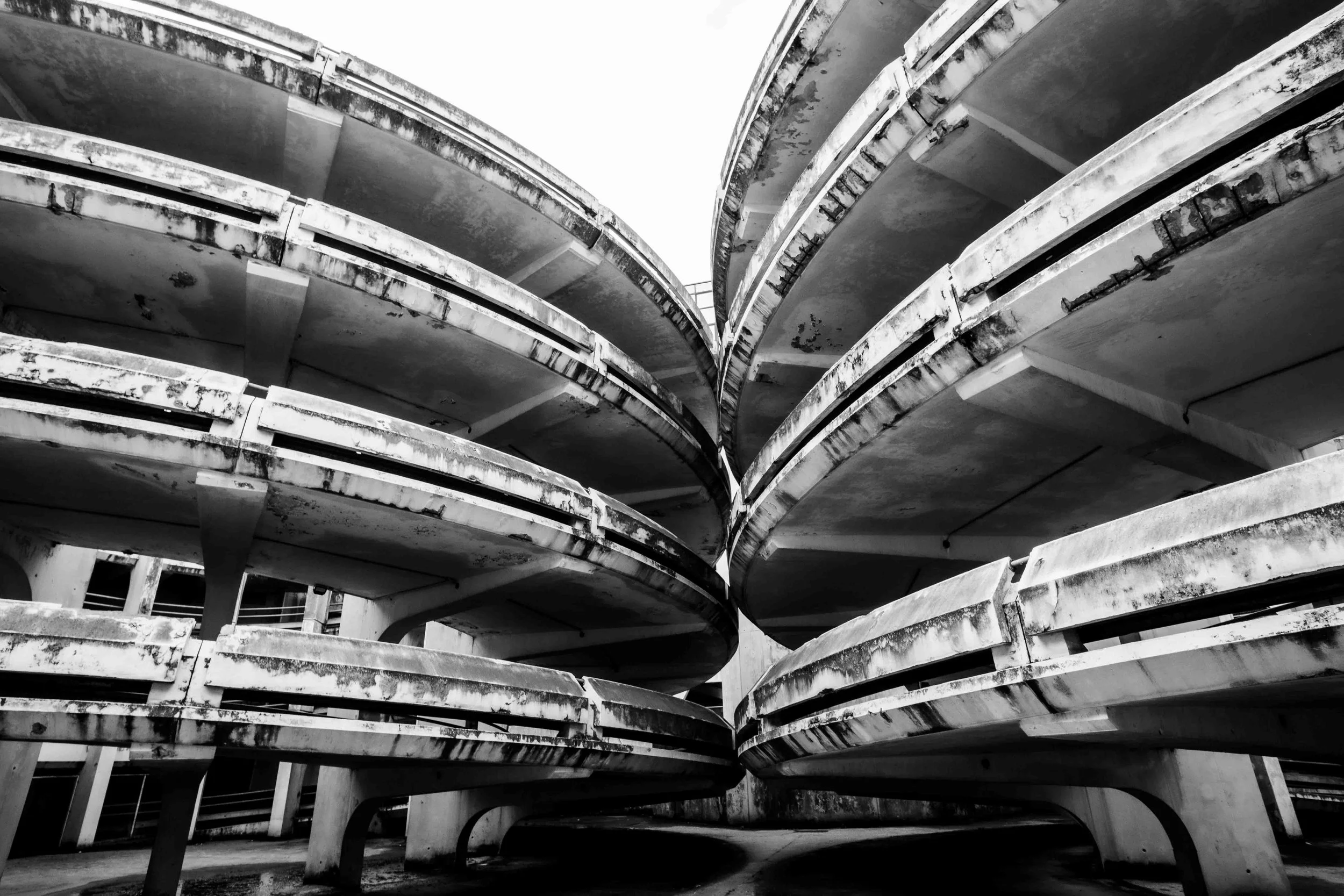 Multiple empty concrete parking garages with curved levels, seen from below, in black and white.