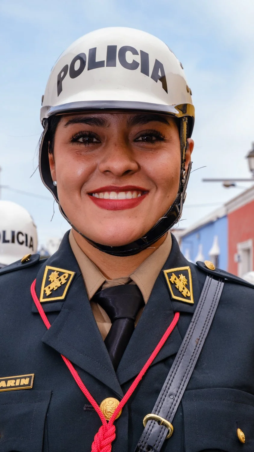 Close-up of a smiling female police officer wearing a white helmet with 'POLICIA' written on it and a dark uniform with insignia.
