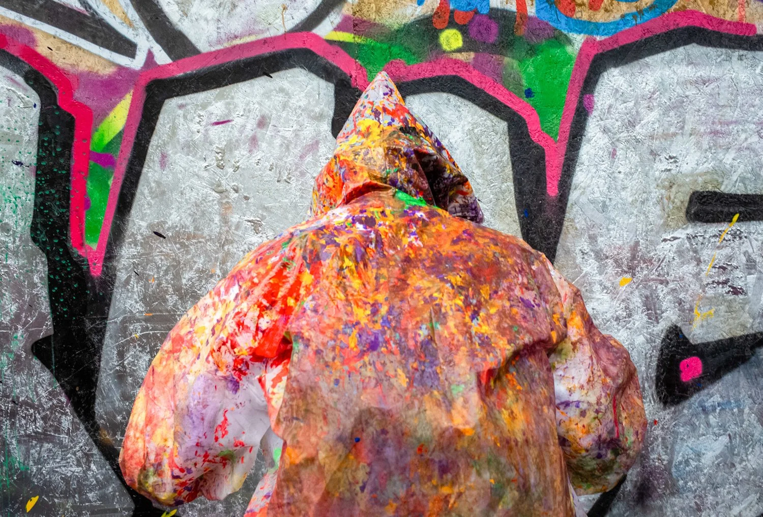 Person wearing a paint-stained hoodie creating graffiti art on a wall.