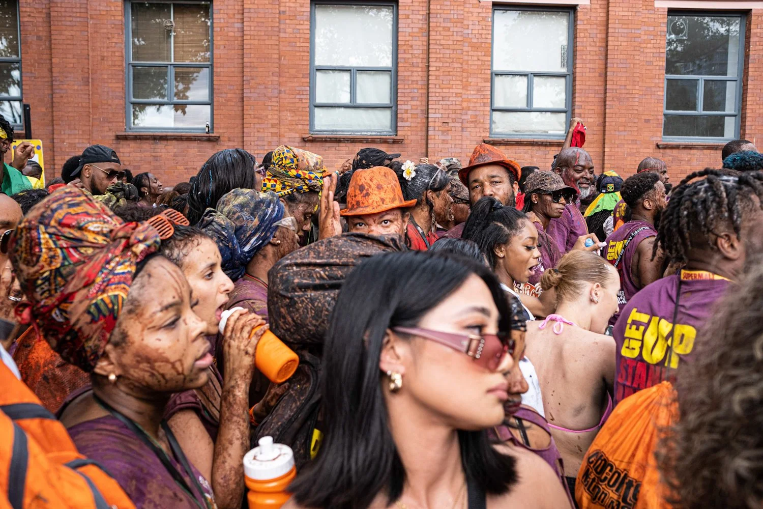 Crowd of people in colorful clothing gathered outside in front of a red brick building.