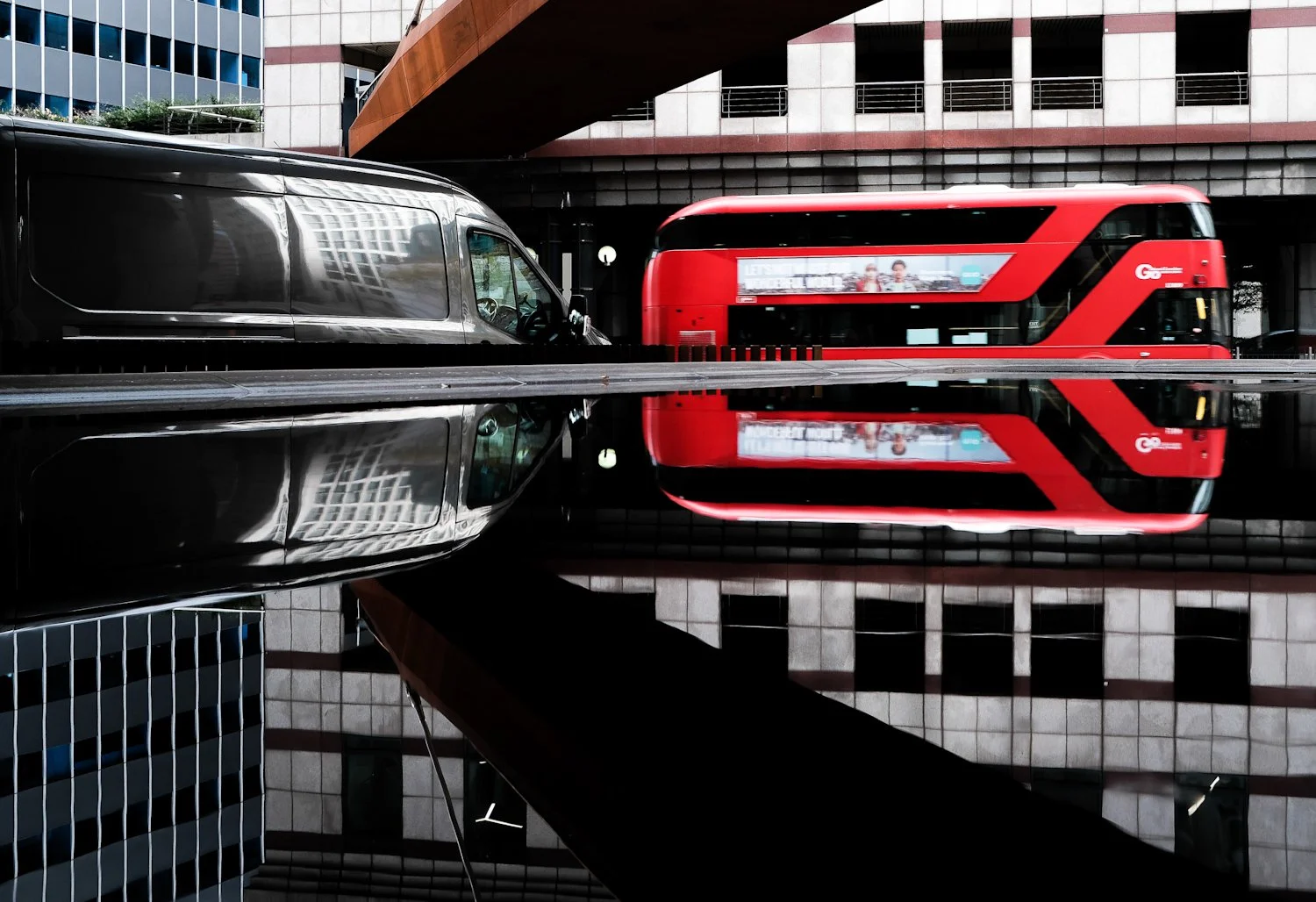 City street scene featuring a red double-decker bus and a reflective black vehicle with surrounding buildings.