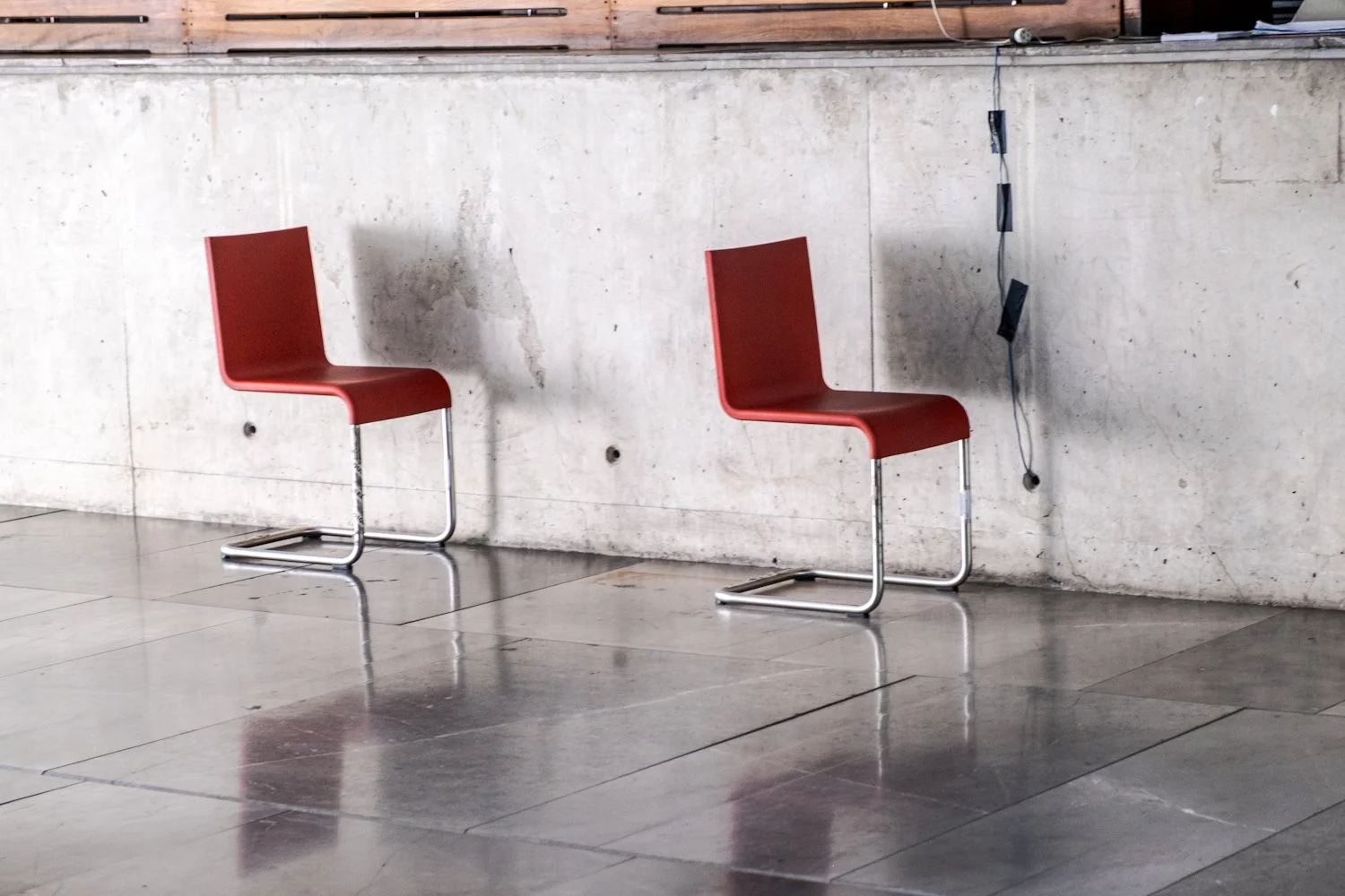 Two red chairs with metal leg frames against a concrete wall in an indoor space.