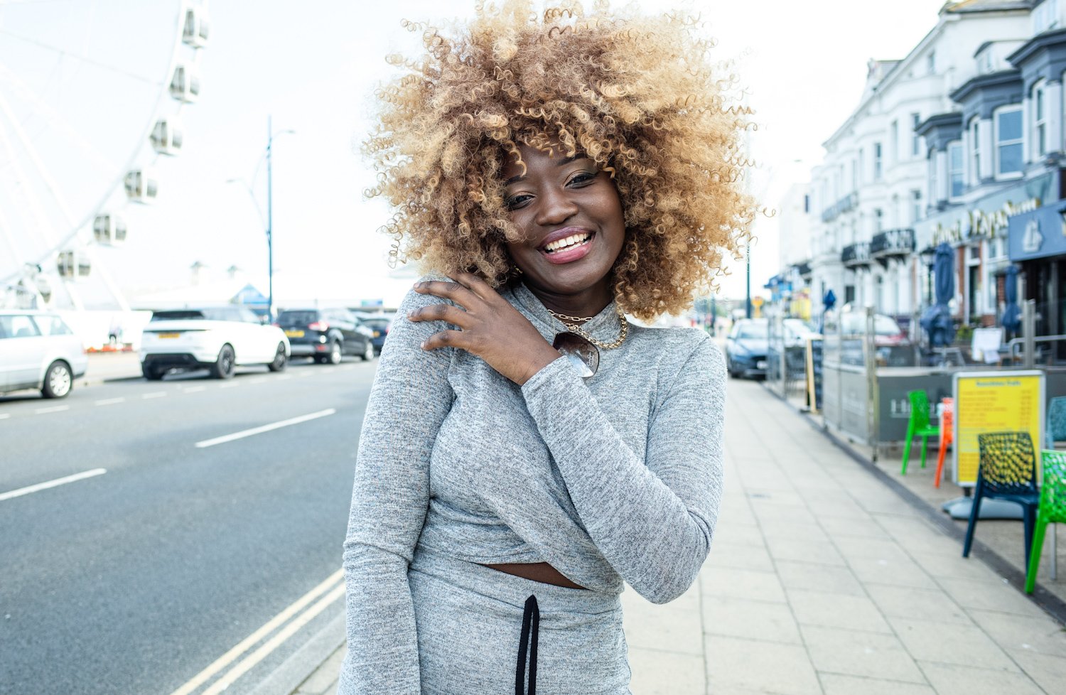 A woman with curly blonde hair smiling on a city street.