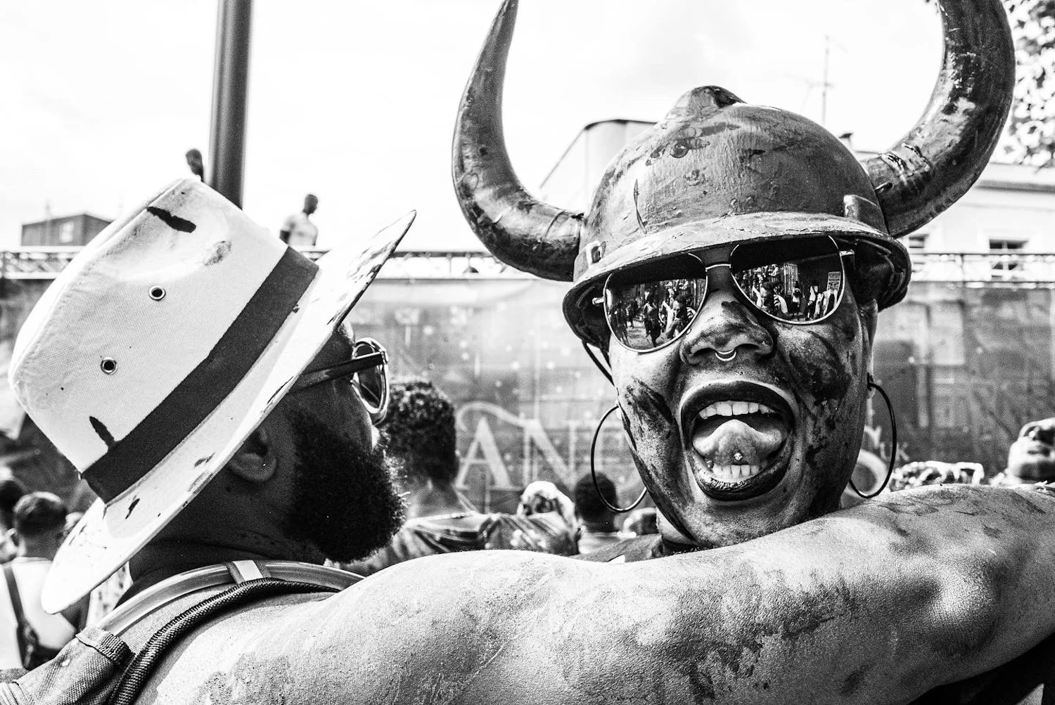 People celebrating outdoors, one woman wearing a Viking helmet with horns and sunglasses, smiling, and embracing another person.