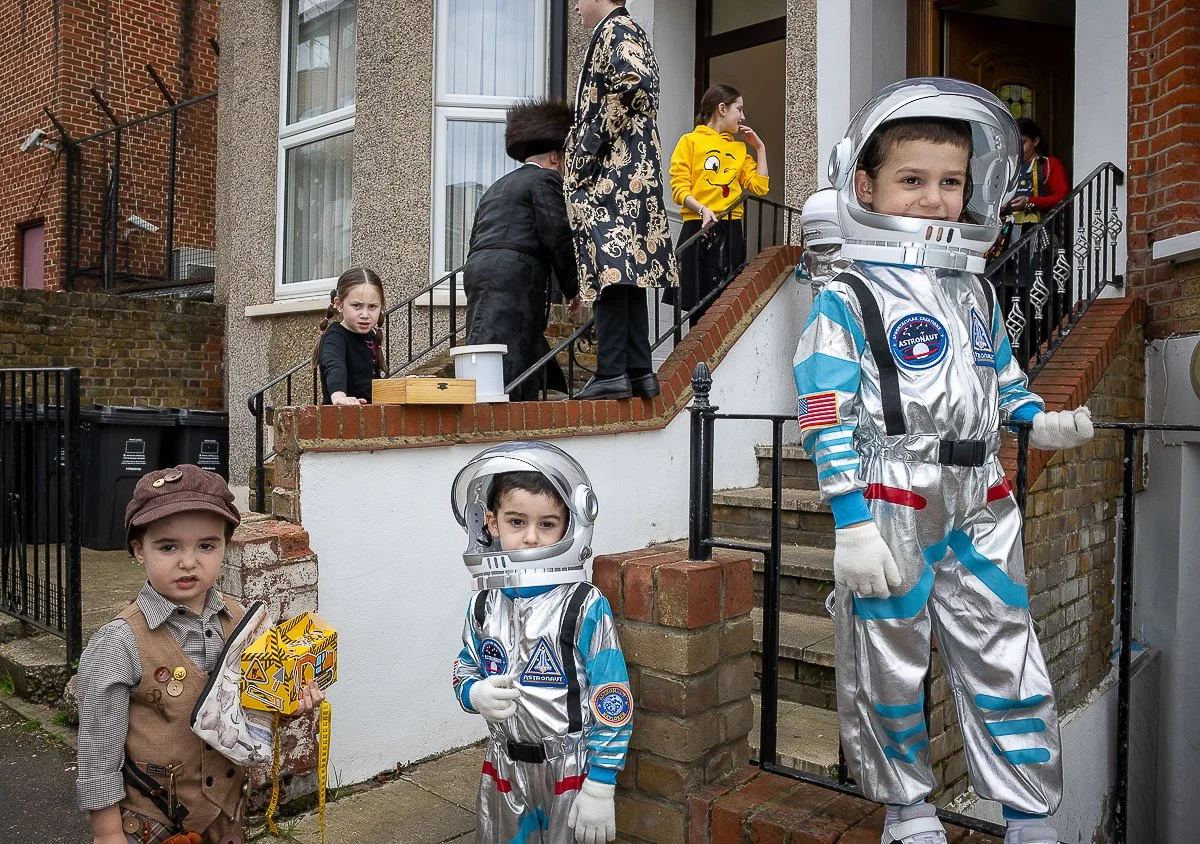 Children dressed in space costumes and holding toys standing outside in a neighborhood.