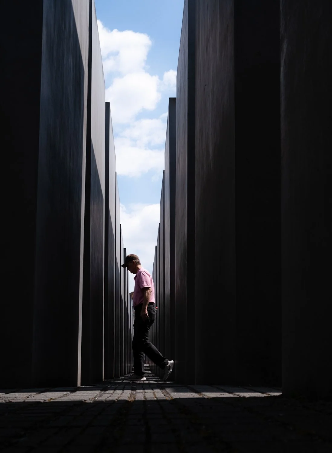 A man walking through the darkened path between tall, black memorial walls at the Memorial to the Murdered Jews of Europe in Berlin.