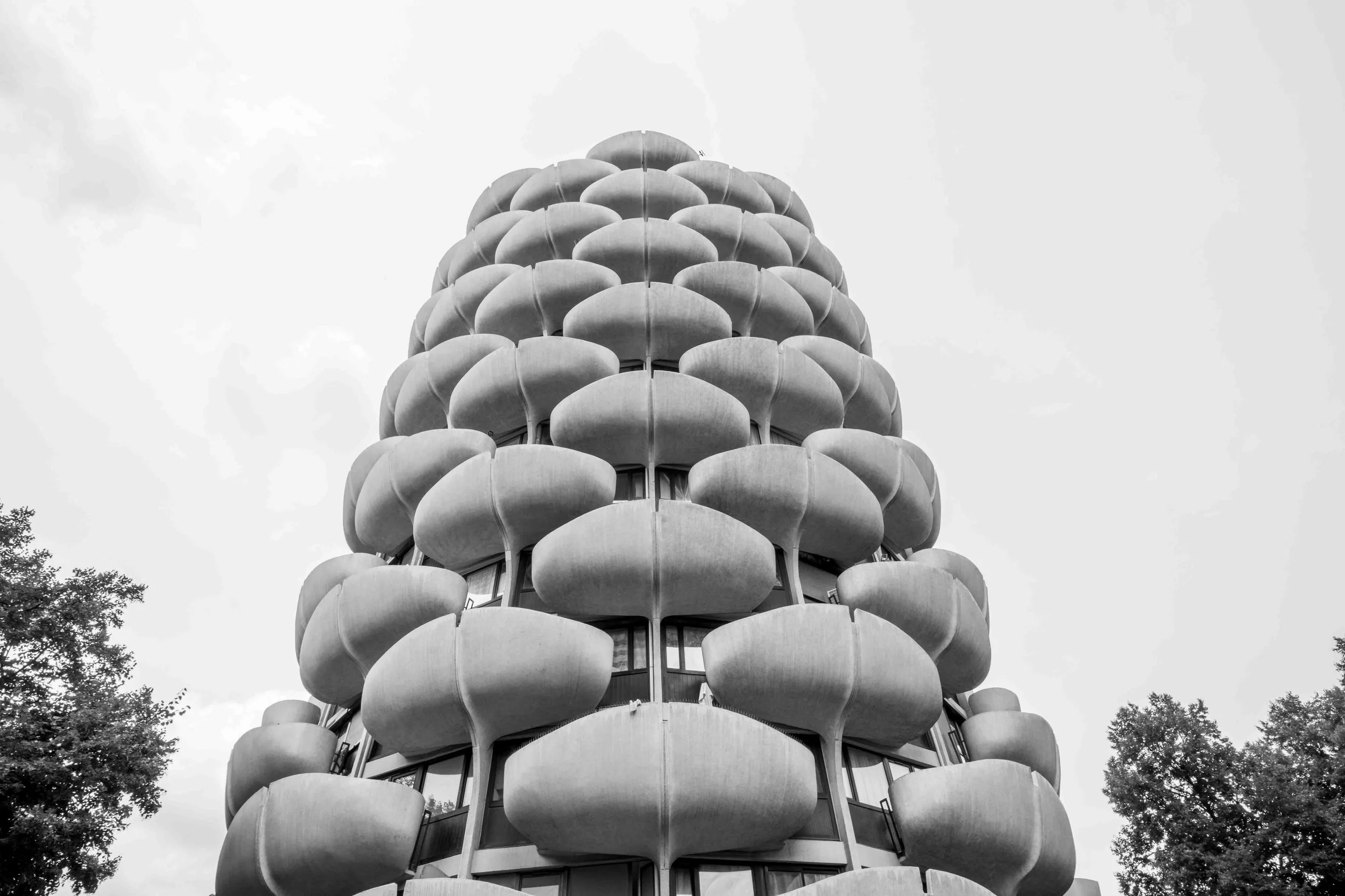 A tall building with multiple rounded balconies stacked vertically, resembling a cone-shaped structure, viewed from below.