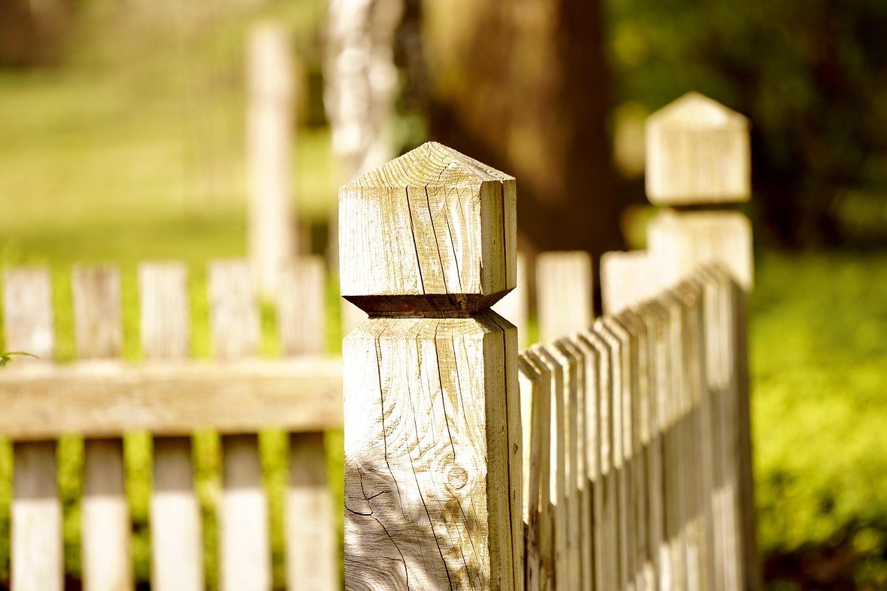 Wooden picket fence with square posts in a sunny outdoor setting.