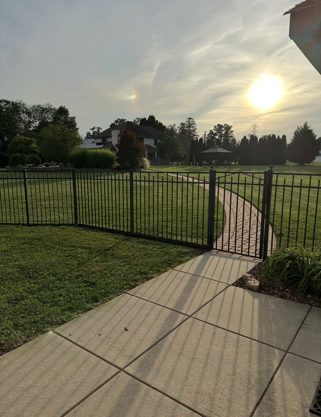 Sunset over a backyard with a gated pathway, green lawn, and trees
