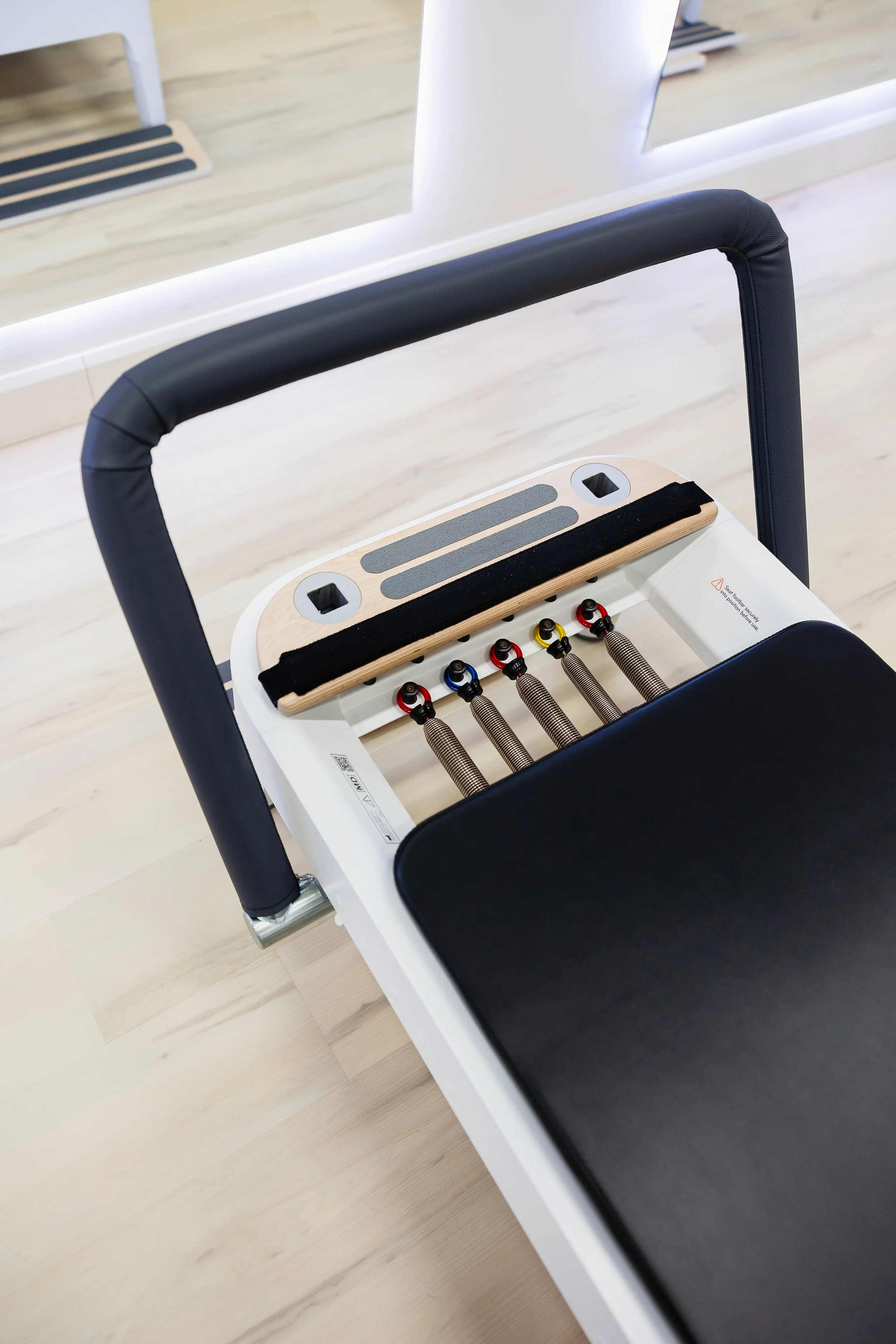 Flooring area with a Pilates reformer machine in a fitness studio with wooden floor and mirror.