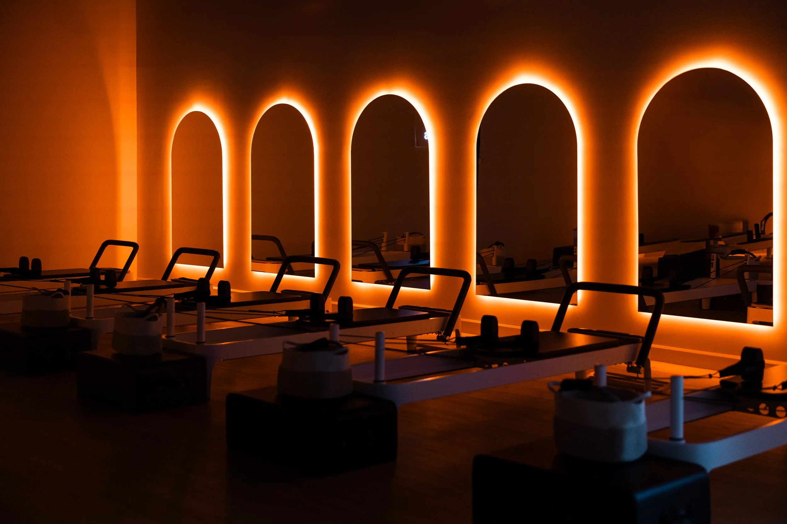 Dimly lit gym room with pilates reformer and orange backlit wall arches