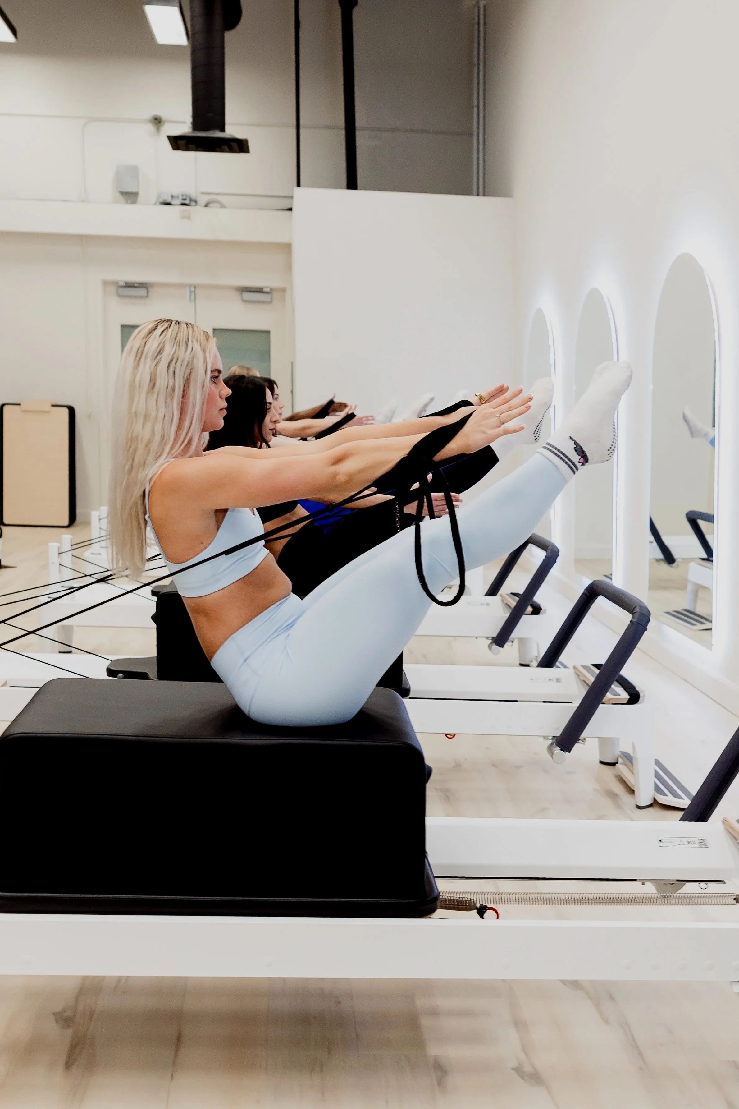 Women with blonde hair and three women with dark hair doing Pilates on reformer machines in a well-lit fitness studio in ottawa