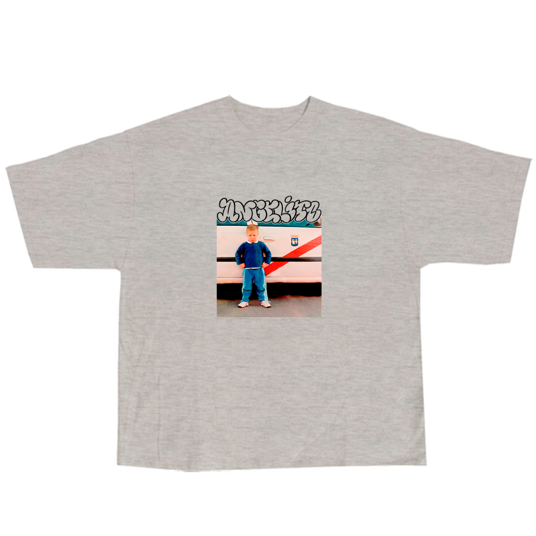 Camiseta gris con una foto de un niño vestido con ropa azul frente a un vehículo de color blanco con rayas negras y rojas, y graffiti en la parte superior.