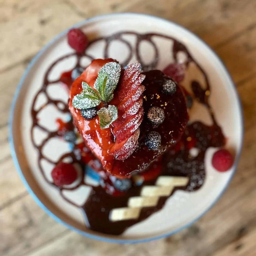Postre con fresas, arándanos y frambuesas cubierto de azúcar glas, decorado con hojas de menta y salsa de chocolate en un plato