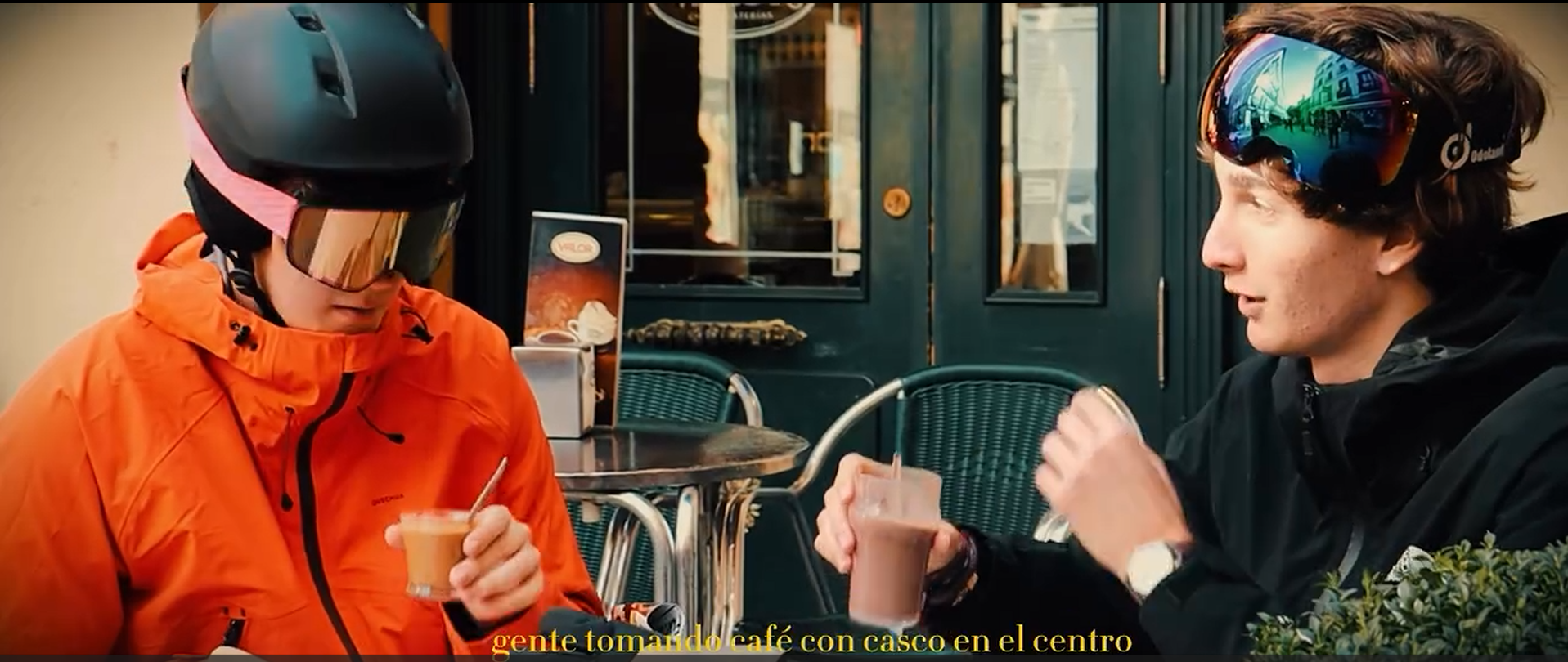 Jóvenes en una cafetería con cascos de bicicleta en la cabeza, tomando café con leche.