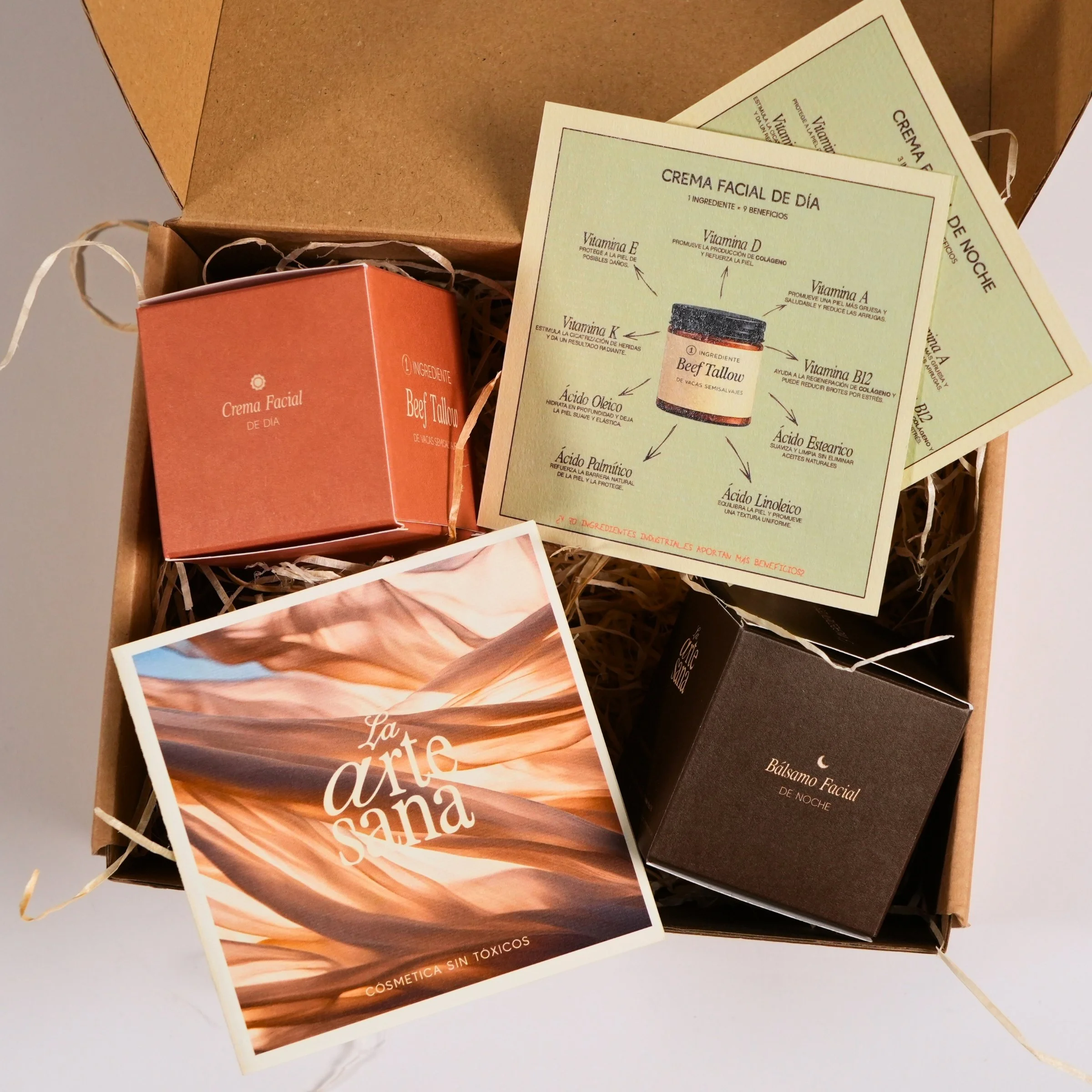 Caja con productos de cuidado facial, incluyendo crema facial de día y bálsamo facial de noche, con folletos informativos y una tarjeta que dice 'La arte sana, cosmética sin tóxicos' en español.