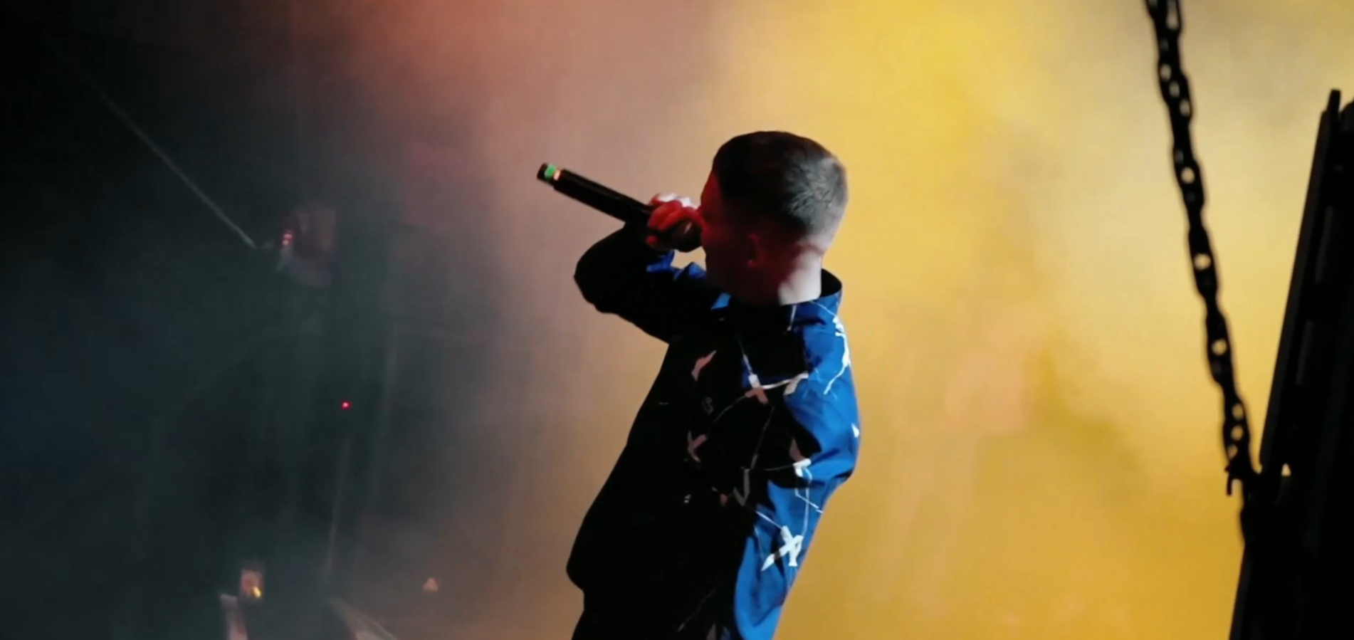 Un niño sosteniendo un micrófono en un escenario con fondo de luces naranjas y oscuras.