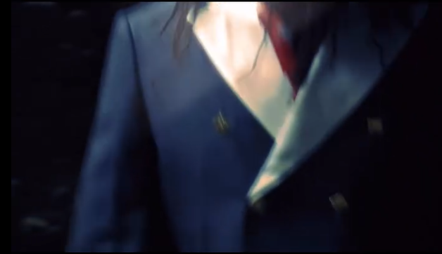 Mujer vestida con saco azul oscuro y blusa blanca, en un entorno oscuro.