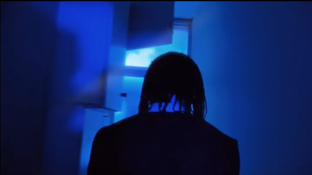 Persona vista desde atrás en una habitación con iluminación azul, de espaldas y con cabello mojado o rizado.